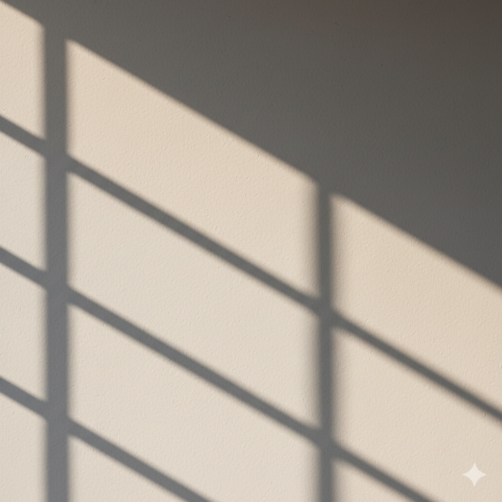 Sunlight casting shadows of a window frame on a textured wall.