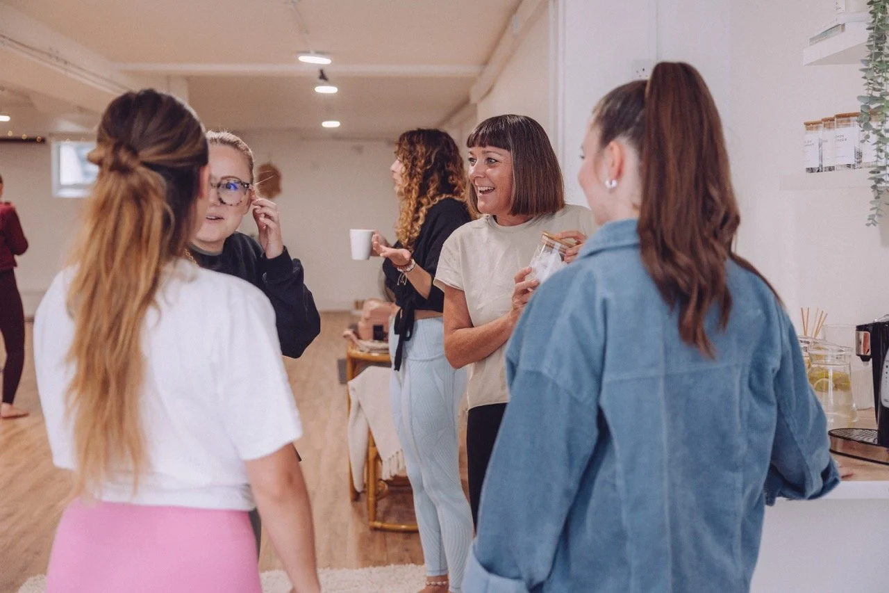 Group of women talking and laughing at a social gathering in a bright living room.