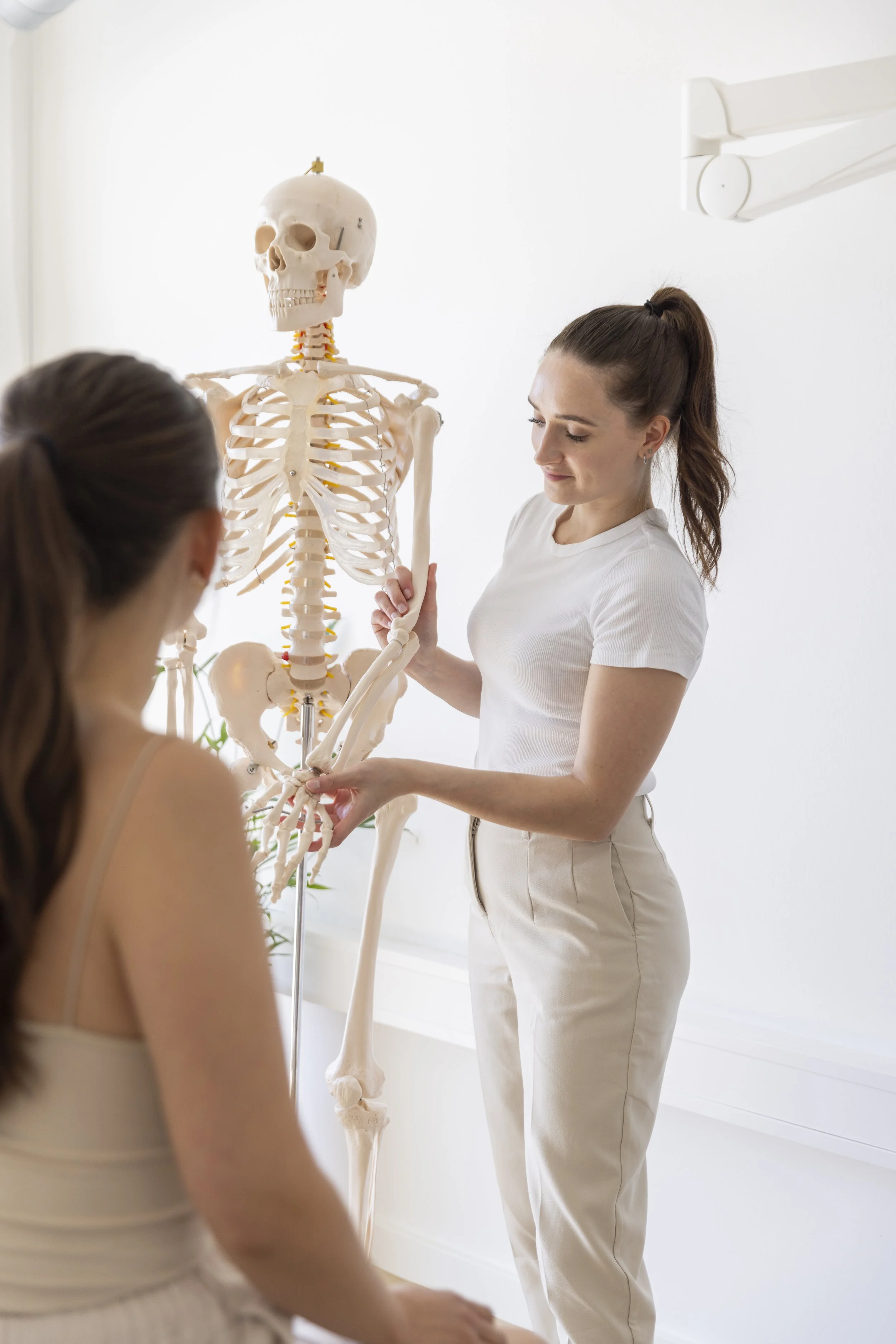 Frau erklärt einer Patientin den menschlichen Skelettaufbau in einer medizinischen Umgebung.