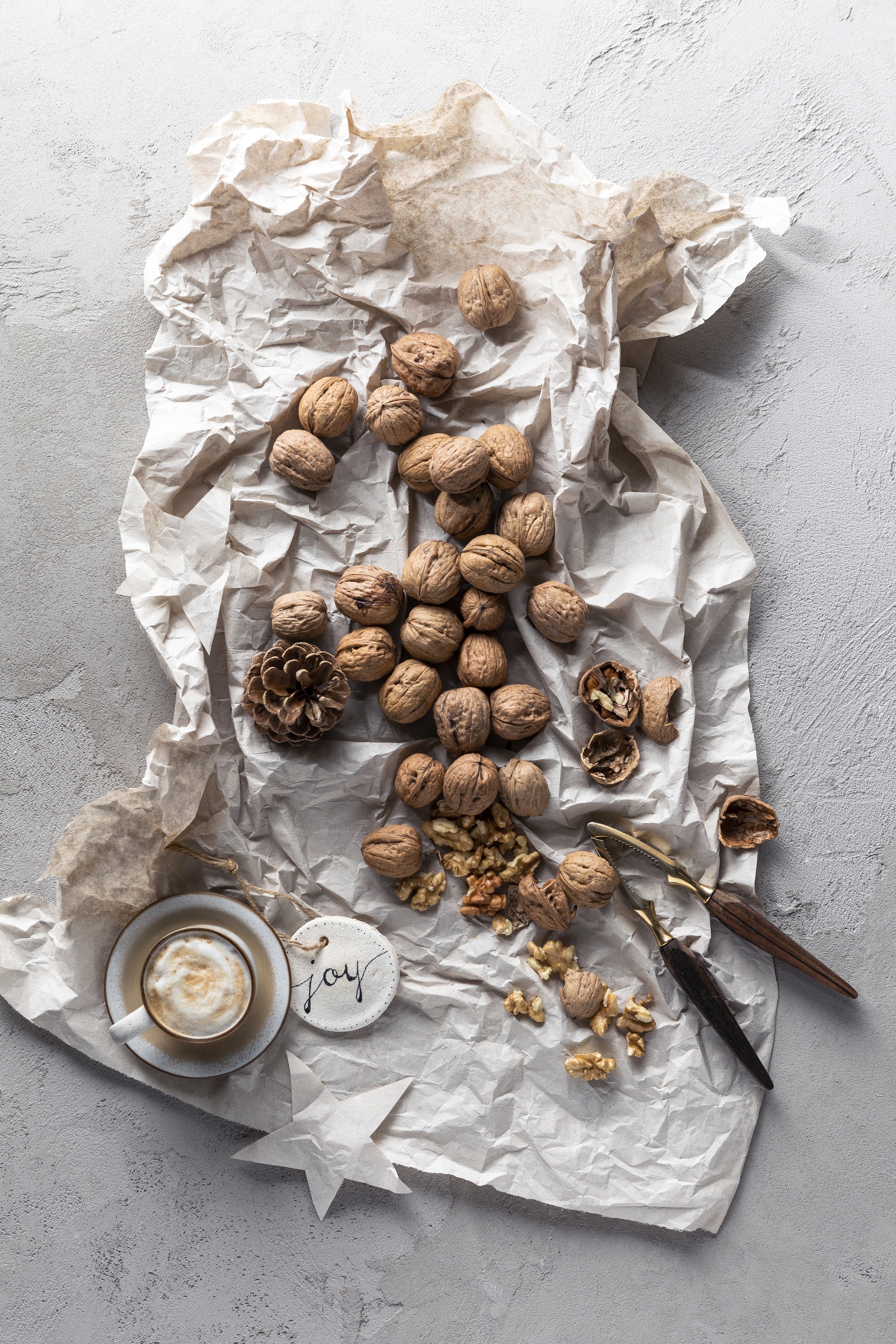 Walnüsse, Tannenzapfen und Nussknacker auf zerknittertem Papier, mit einer Tasse Kaffee mit Schaum und einem "joy"-Anhänger