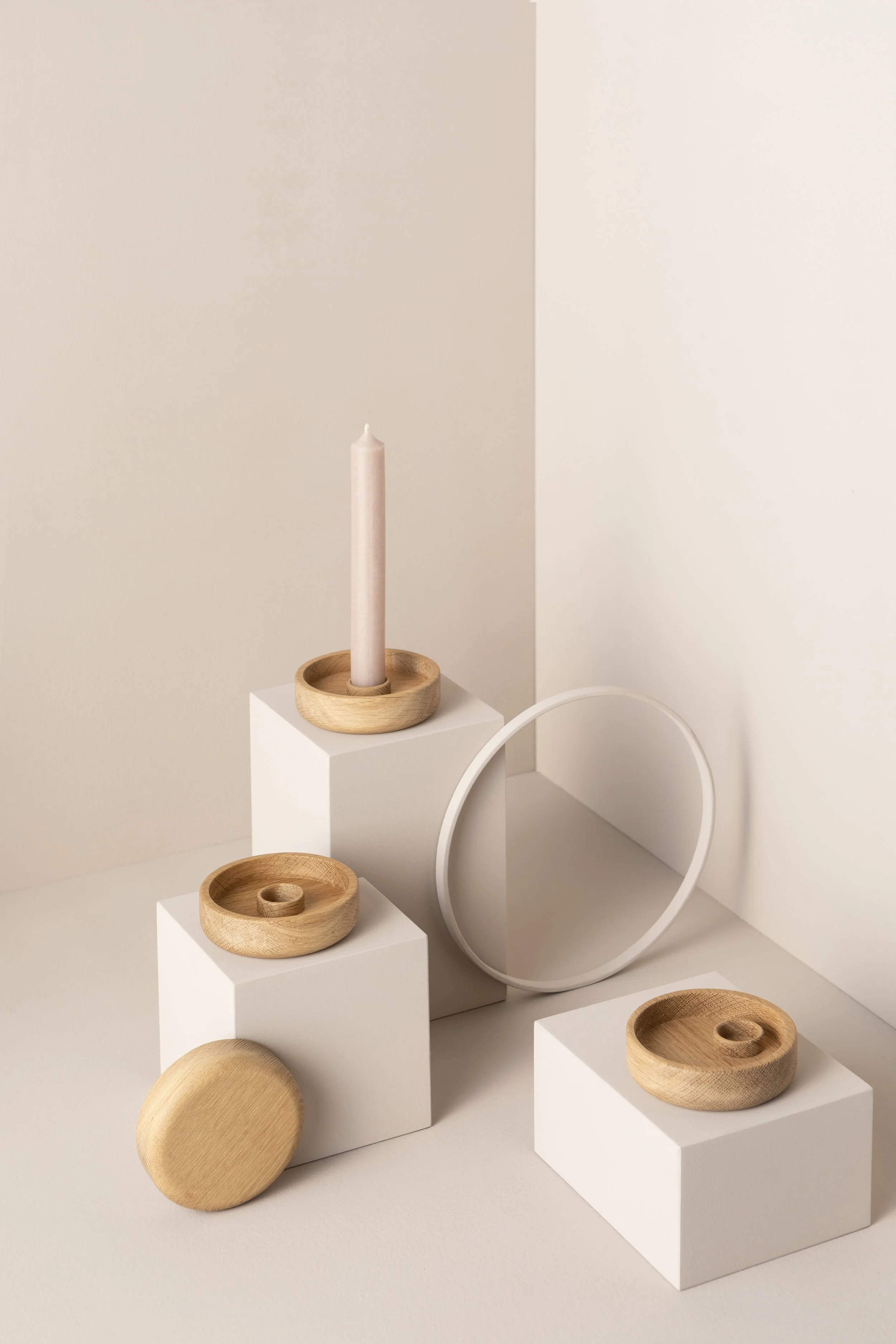 Minimalistisches Dekor mit Kerzen, Holzschalen und einem runden Spiegel auf weißen Würfeln gegen eine helle Hintergrundwand.