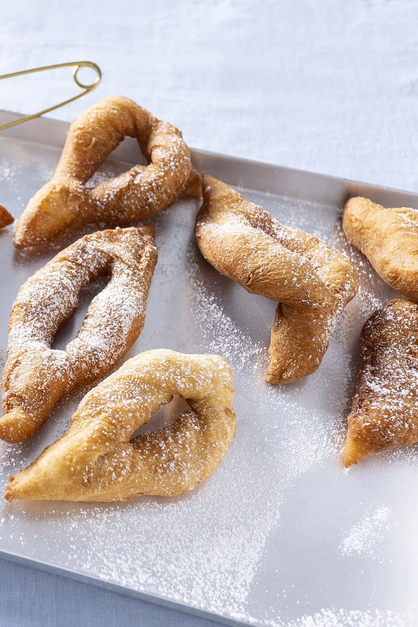Frittierte Kubba, die mit Puderzucker bestäubt sind, auf einer silbernen Oberfläche serviert.