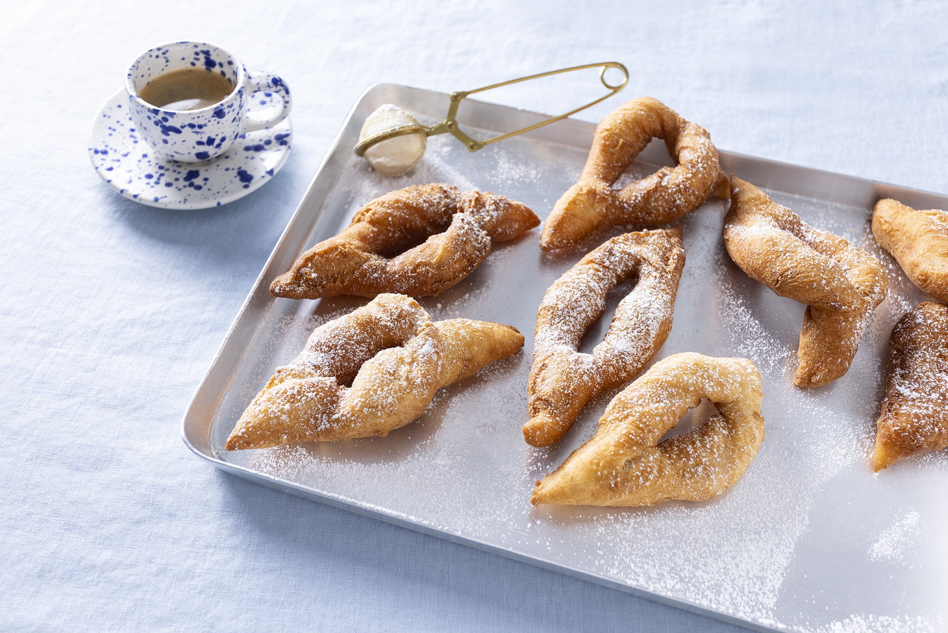Gefüllte Krapfen auf einem Metalltablett mit Zimt- und Puderzuckerguss, daneben ein Teller mit Kaffee.