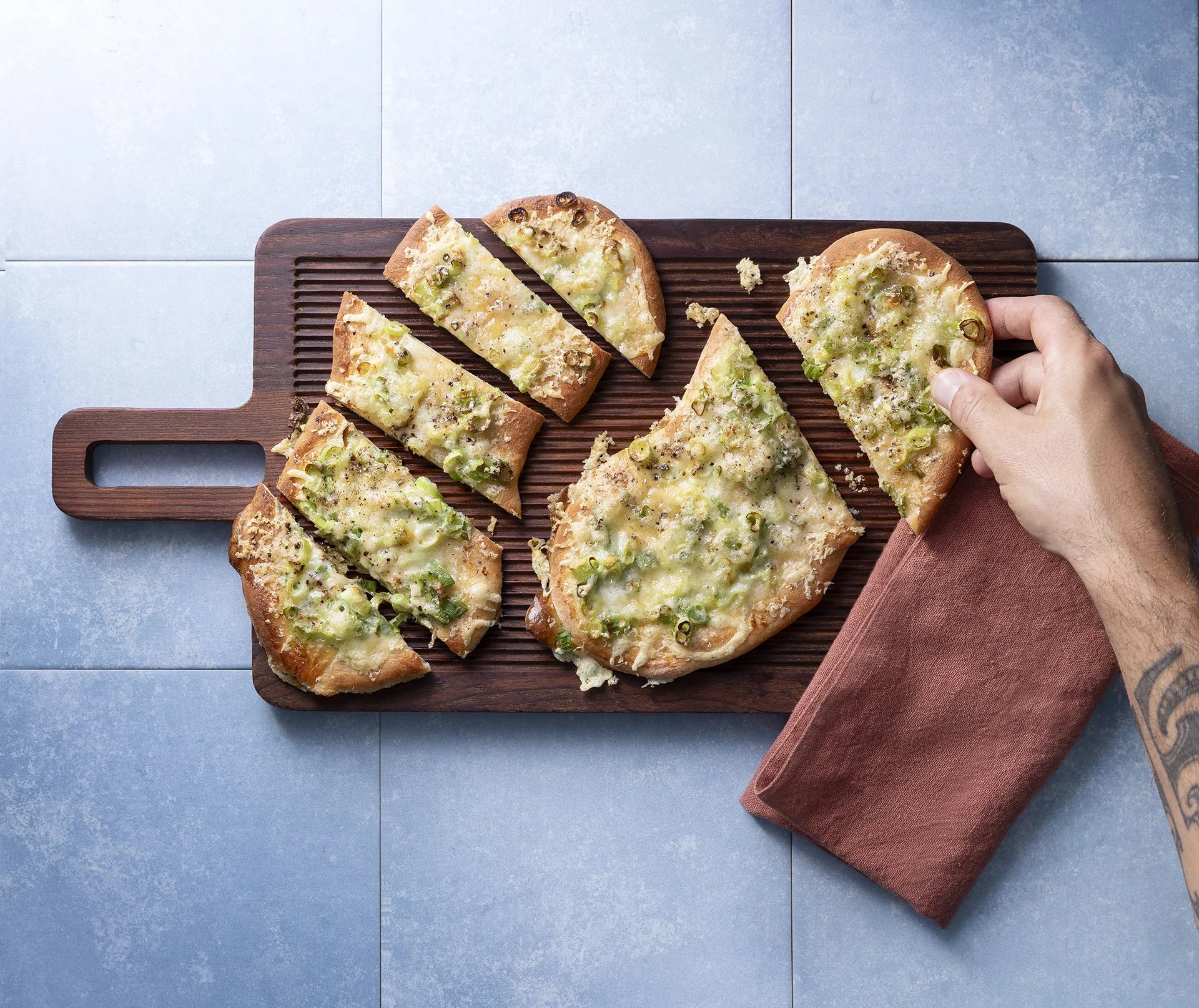 Brot mit Käse und Frühlingszwiebeln auf Schneidebrett, eine Hand hebt ein Stück