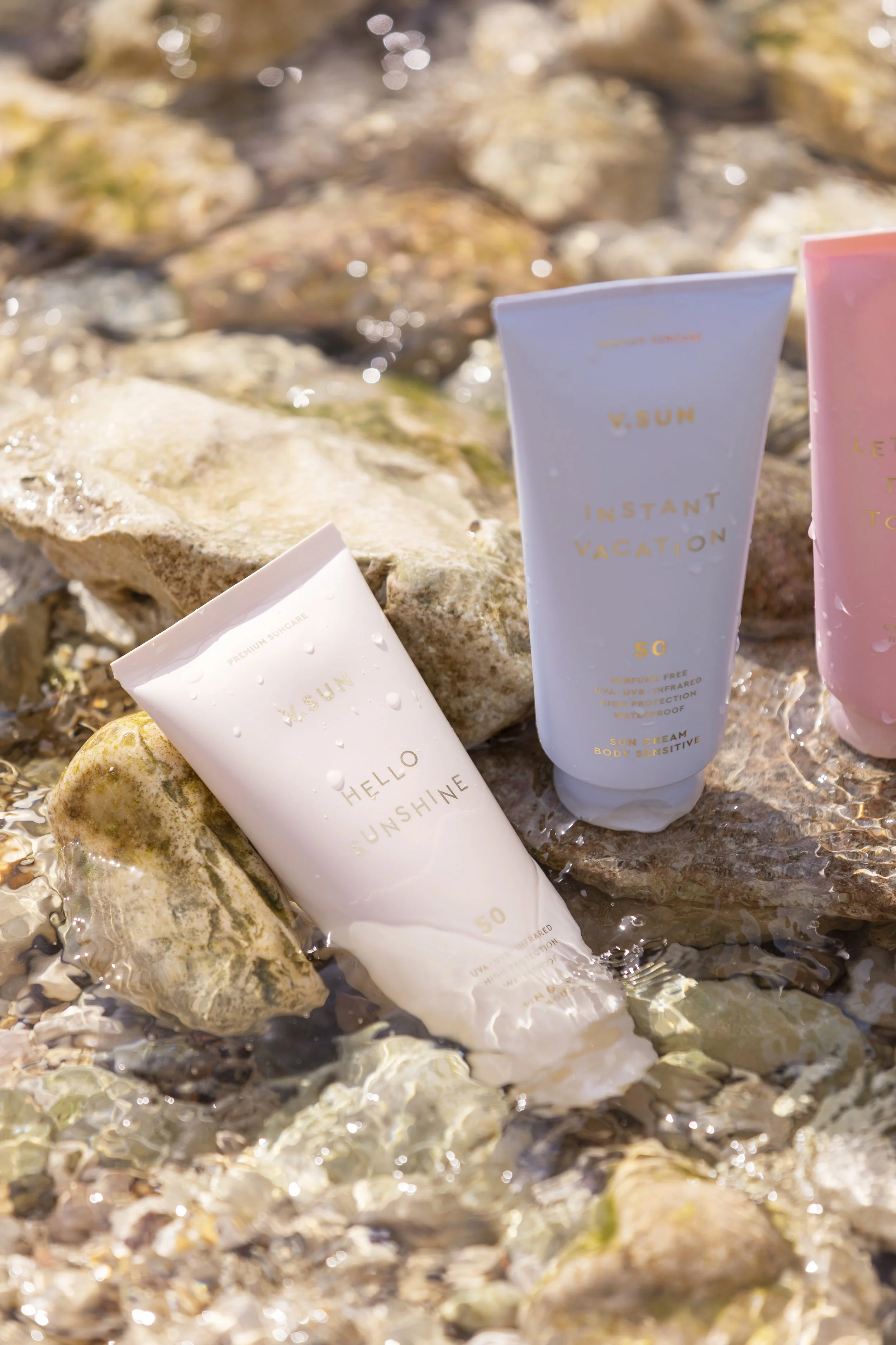 Sonnenschutzcreme in drei Tuben, die in Wasser auf Steinen liegen, bei Sonnenlicht.