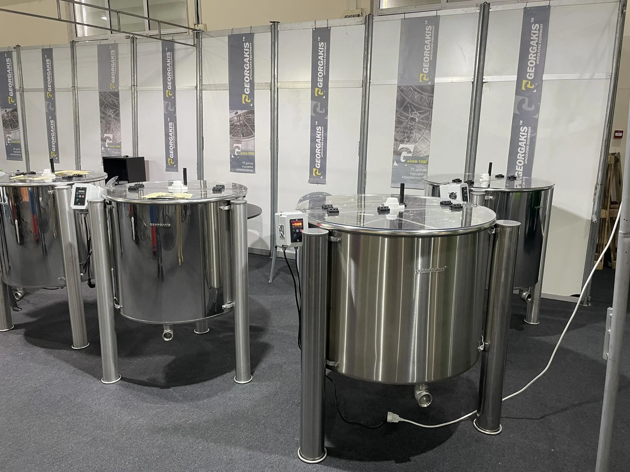 Several large stainless steel industrial machines, likely dough mixers, displayed in a trade show booth with banners that have the brand name 'GEORGAKIS' on a white background.