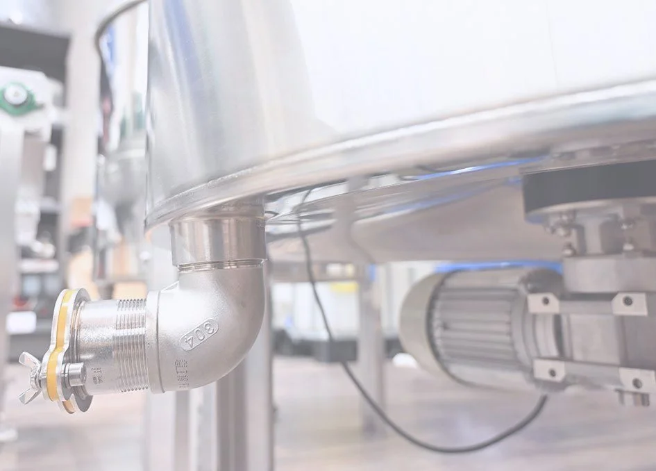 Close-up of a stainless steel pipe with a valve, part of industrial equipment or machinery in a factory setting.
