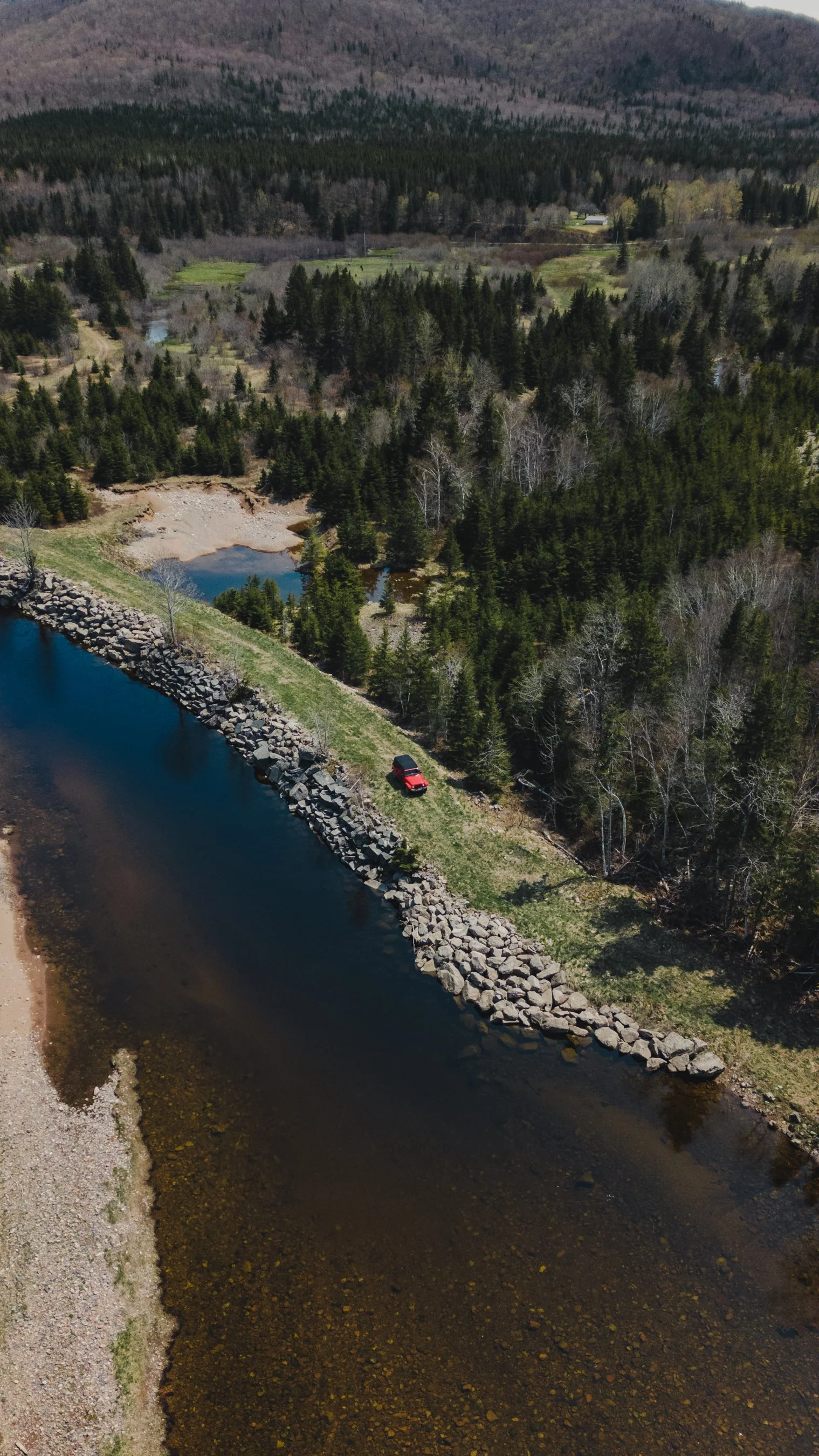 Aerial view of a lake with rocky shoreline, surrounded by trees and hills in the distance.