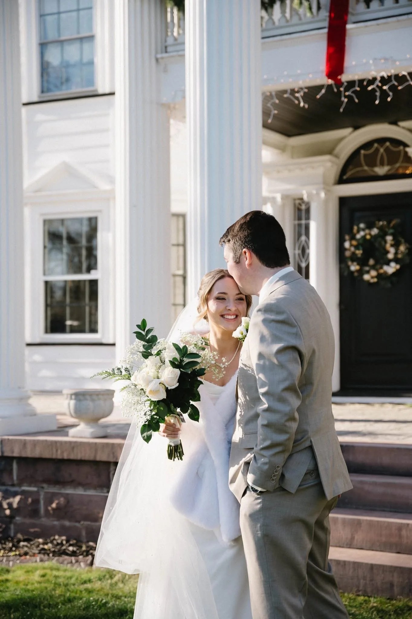 Smiling bride holding a bouquet outside an elegant mansion