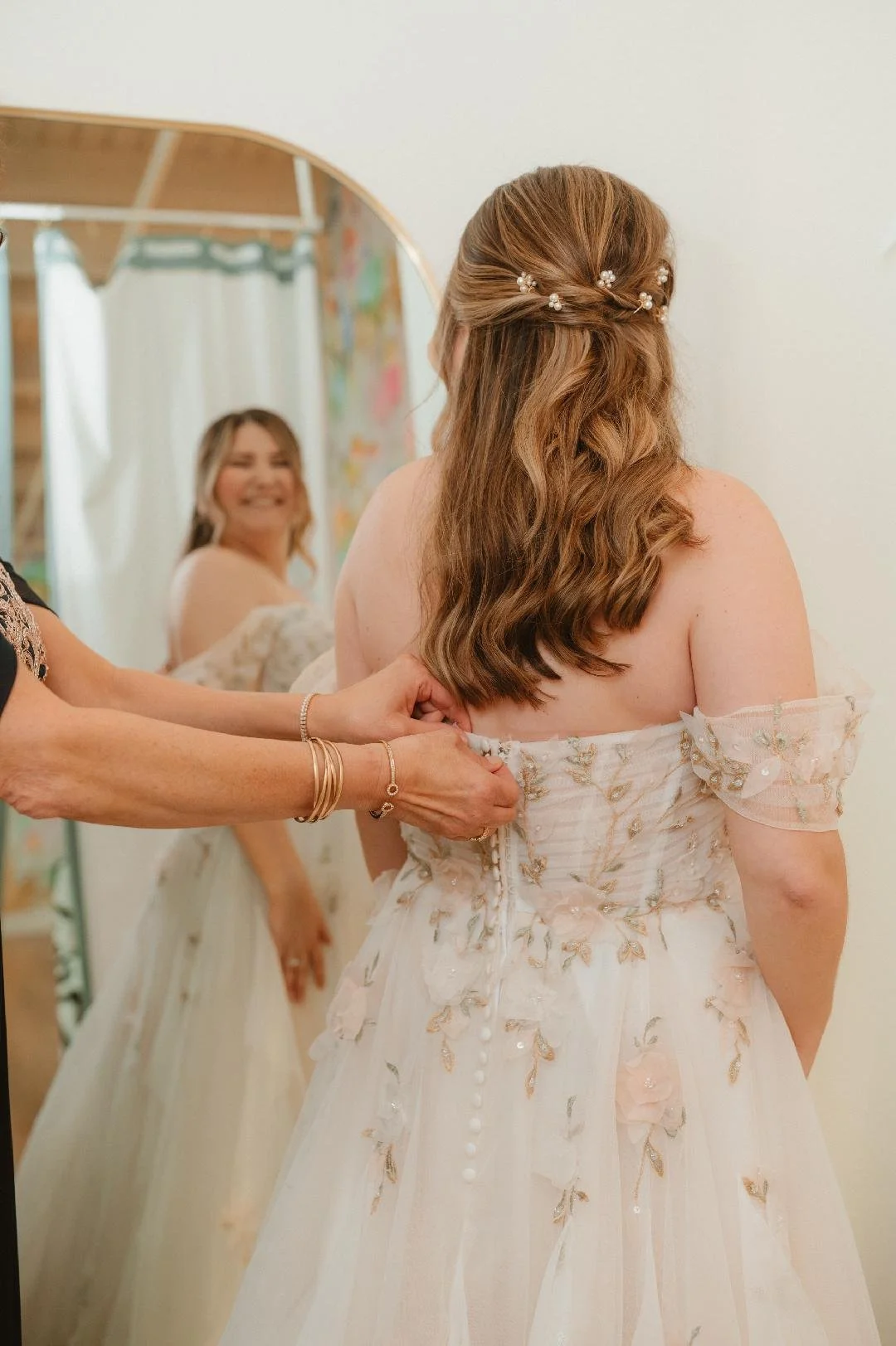 Bride getting ready while her finished hairstyle is reflected in a mirror