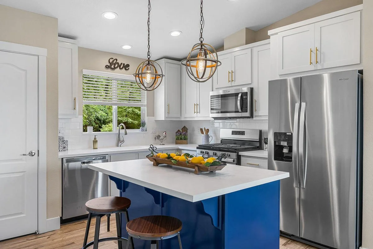 Modern kitchen with white cabinets, stainless steel appliances, a blue island with a white countertop, two wooden stools, and decorative lighting fixtures.