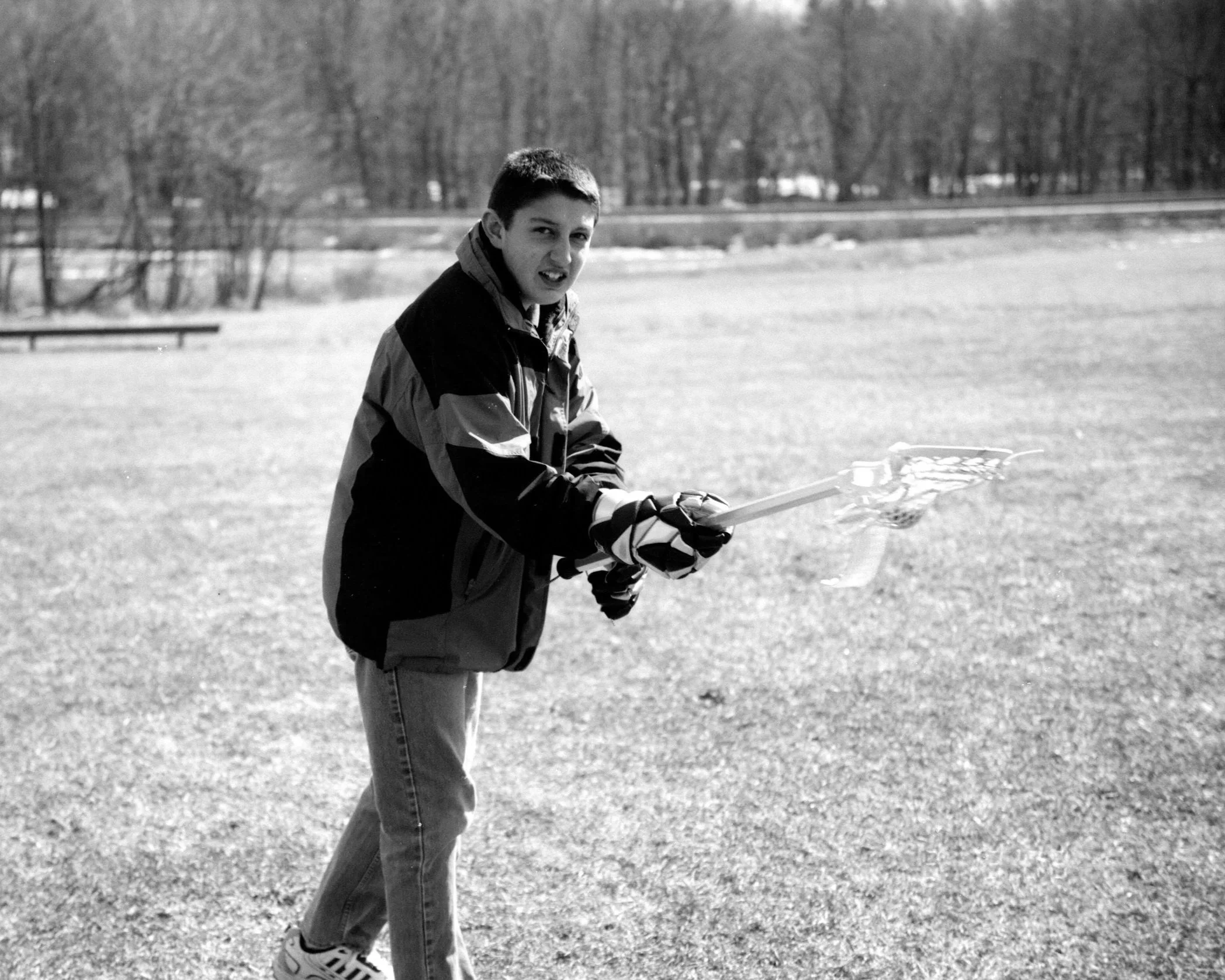 A young boy standing on grass holding a lacrosse stick outdoors.
