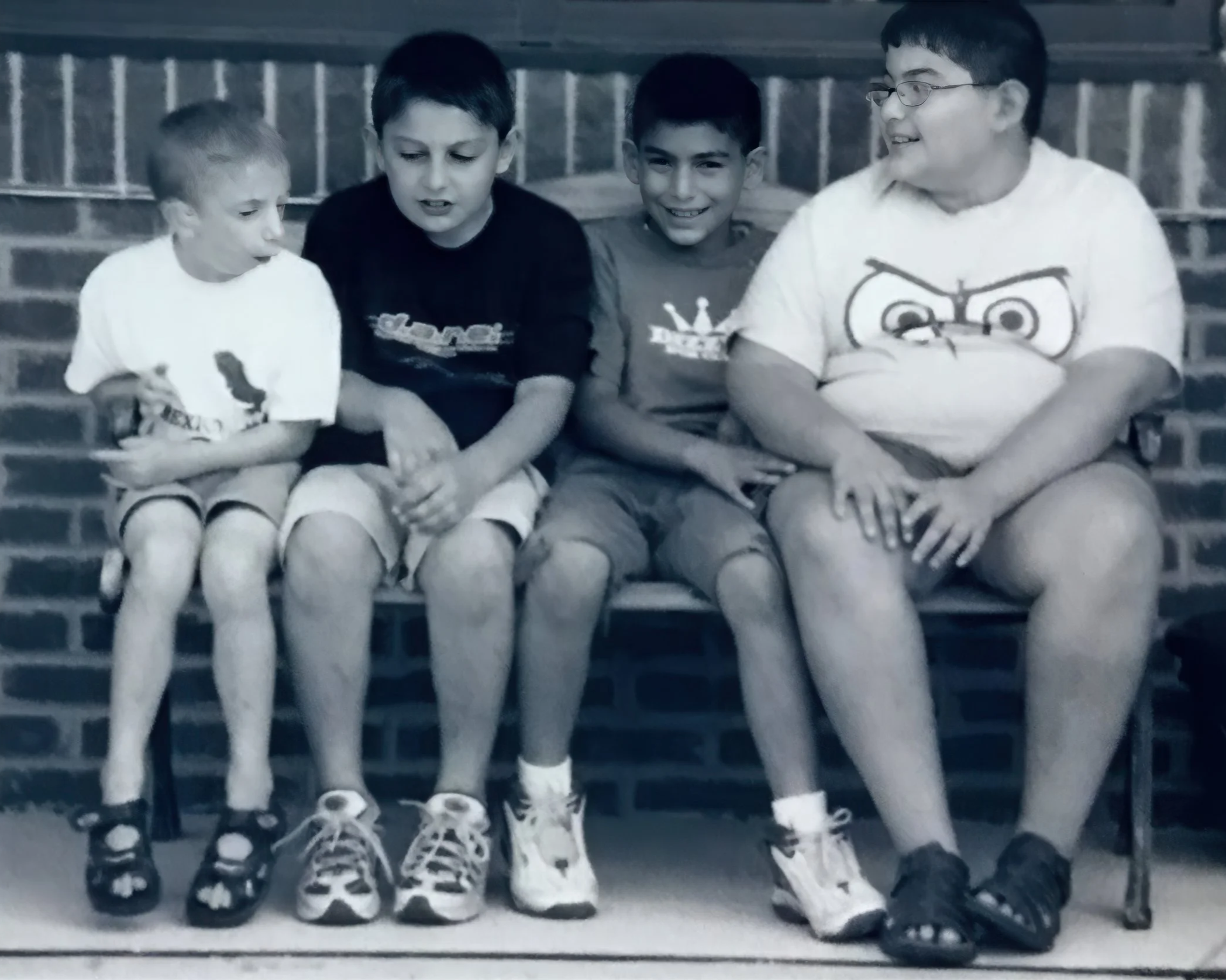 Four boys sitting on a bench against a brick wall, two of them are looking at something and two are smiling.