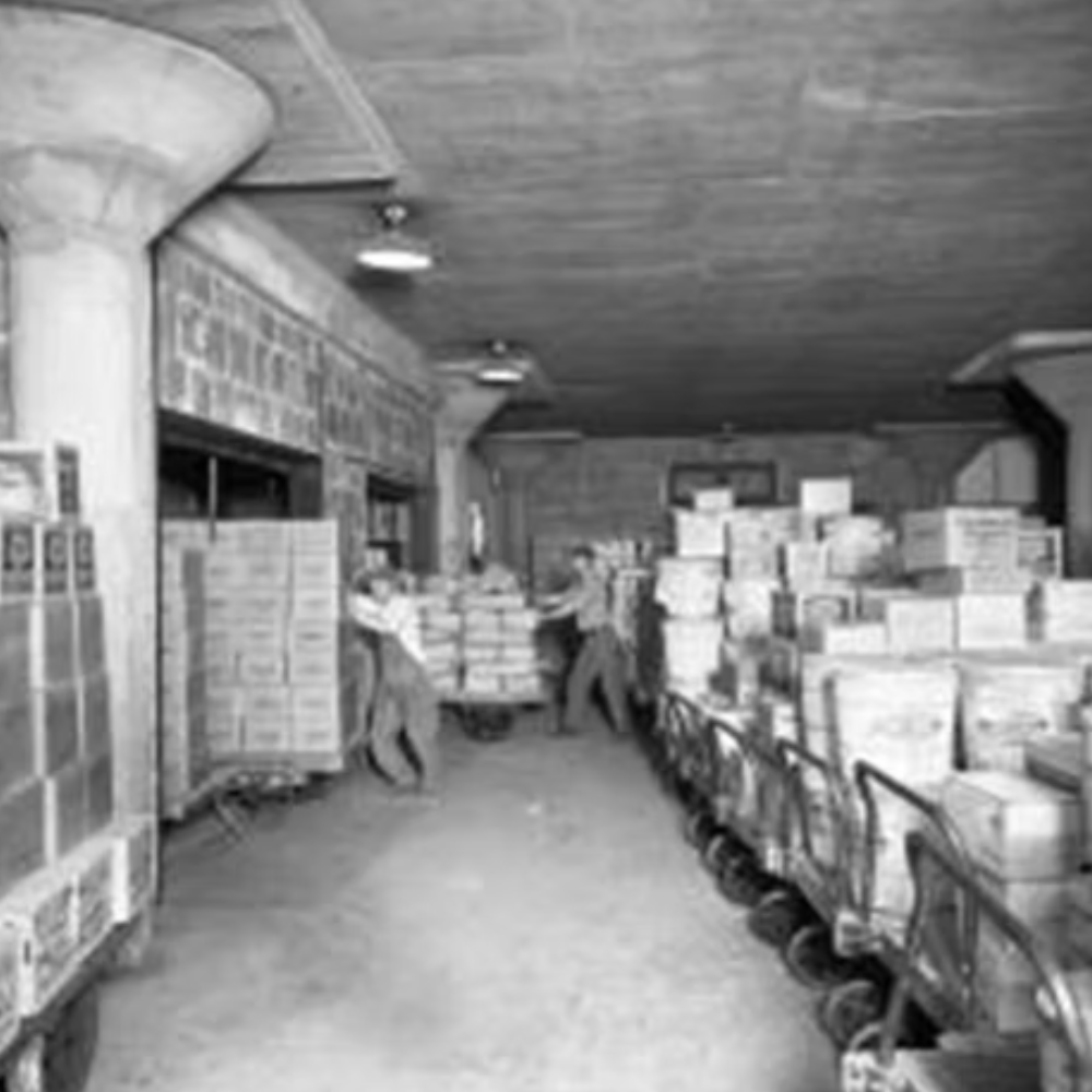Warehouse or storage area with stacks of boxes and workers handling the boxes on carts.