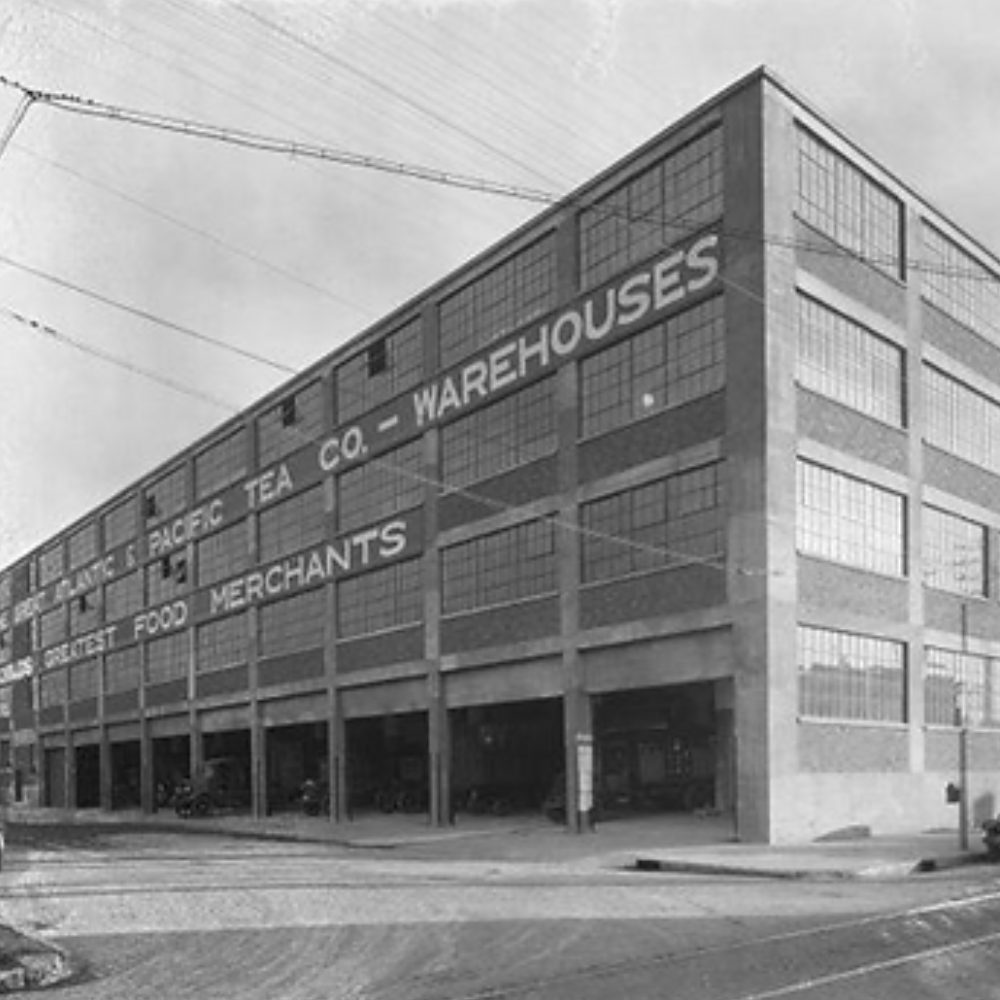 Black and white photo of a large, multi-story warehouse building with a sign reading 'GREAT LAKES RICE & TEA CO. - WAREHOUSES' and 'GROCERY, FOOD, MERCHANTS' on the side.
