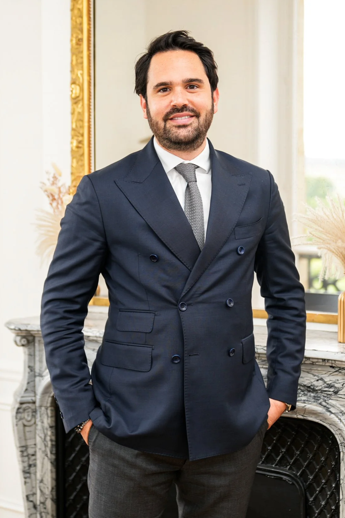 Michaël Pachter, directeur général de Kays Wealth Management en costume sombre, cravate grise, posant dans un intérieur élégant avec un miroir doré et une cheminée en marbre.