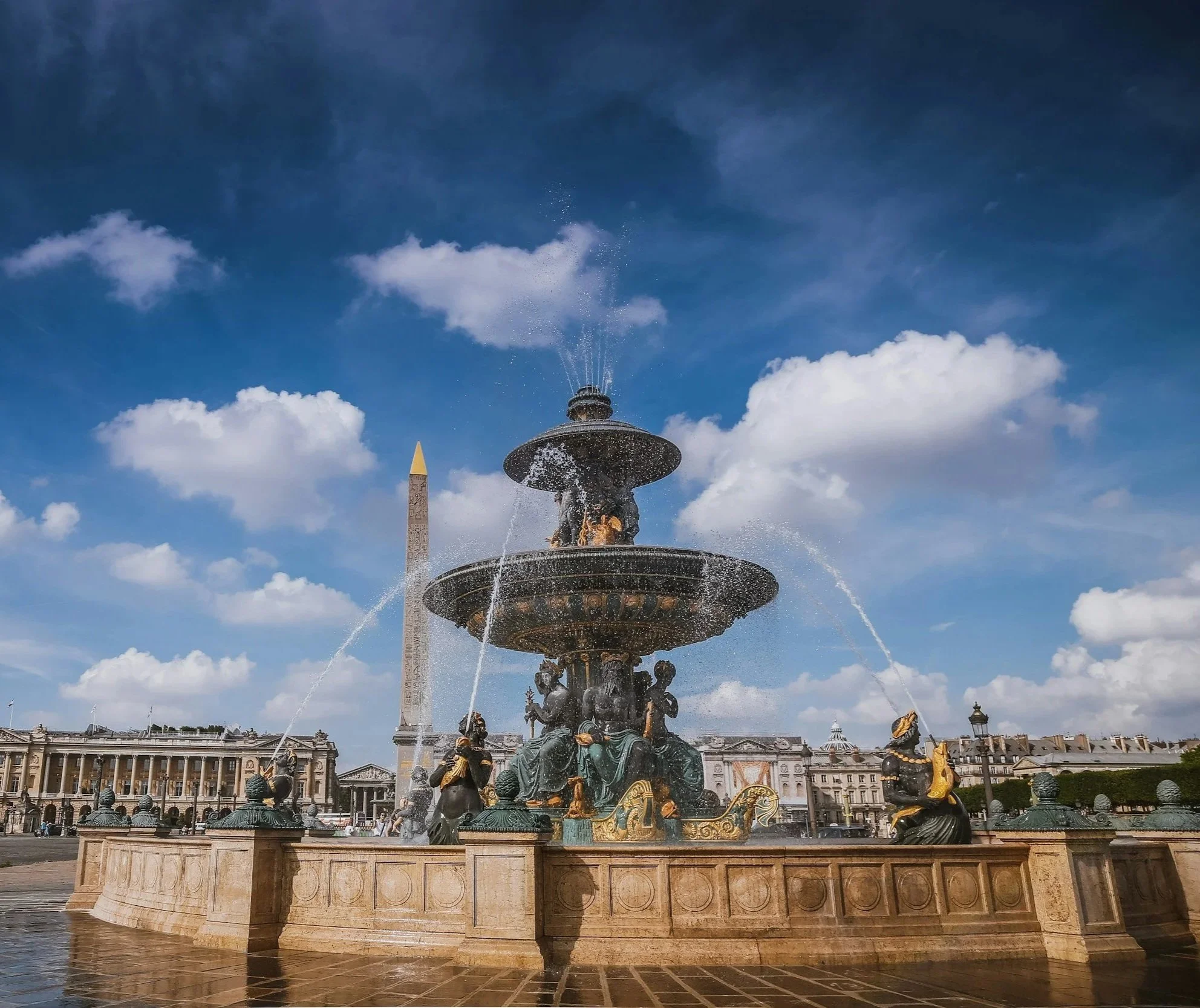 Place de la Concorde à Paris, proche des bureaux de Kays Wealth Management. Une fontaine ornée de sculptures en bronze d'animaux et de figures mythologiques, avec un ciel bleu parsemé de nuages blancs et une obélisque en arrière-plan.