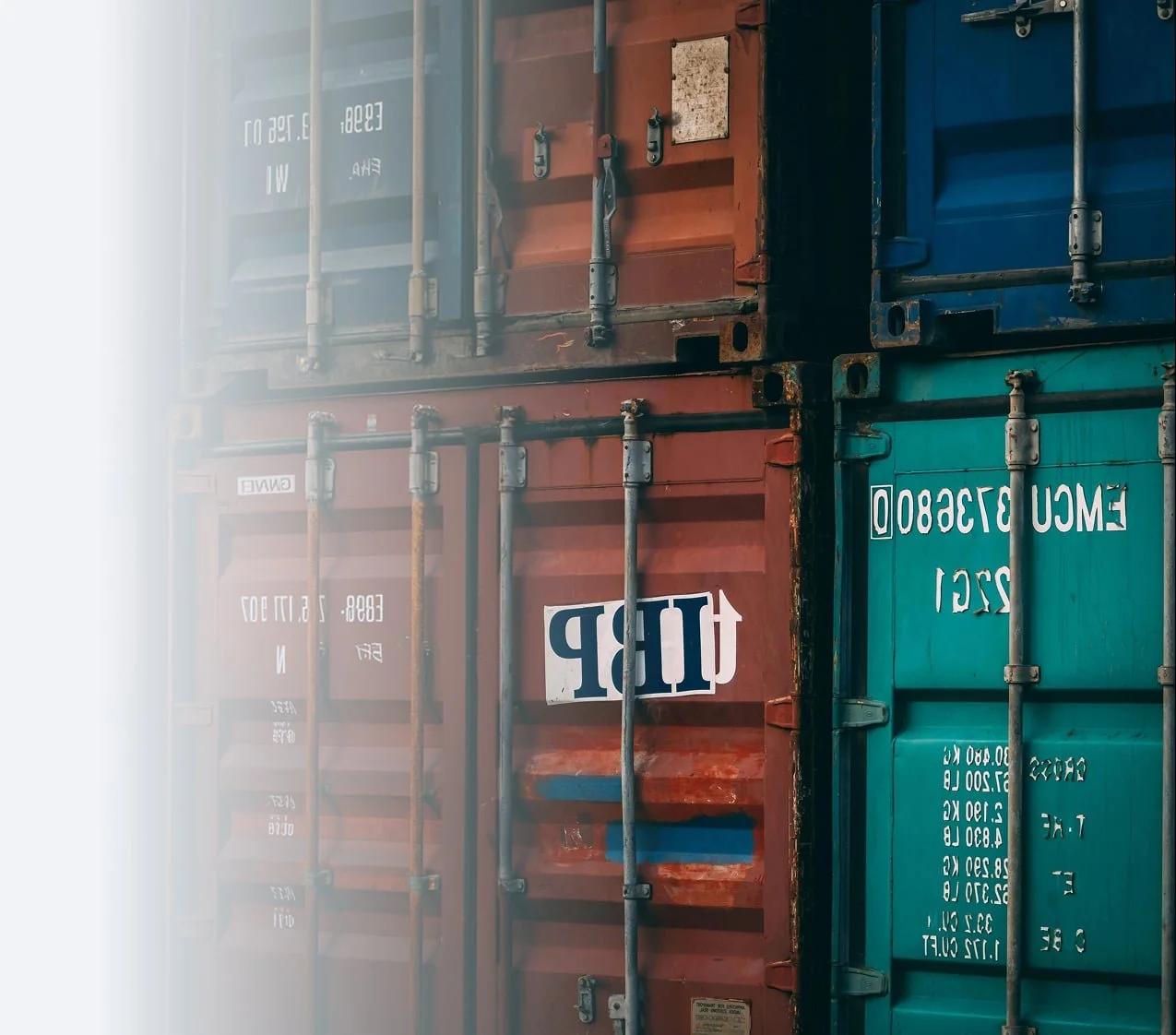 Stacked shipping containers in red, green, and blue with visible metal locking bars and white stenciled text.