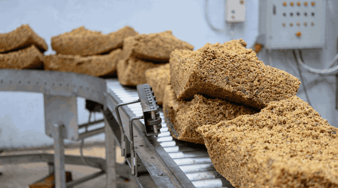 Baked bread loaves on a conveyor belt in a bakery or industrial kitchen setting.