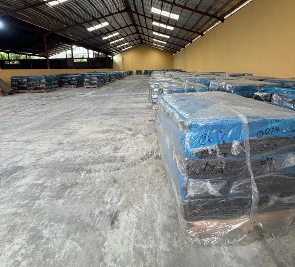 Empty warehouse with industrial roof and stacked wrapped packages on pallets, possibly for storage or distribution.