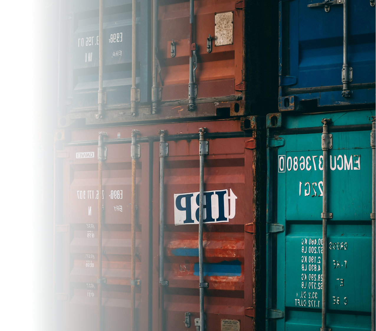Close-up of stacked shipping containers, mostly red with some blue and green, with visible metallic locks and hinges.