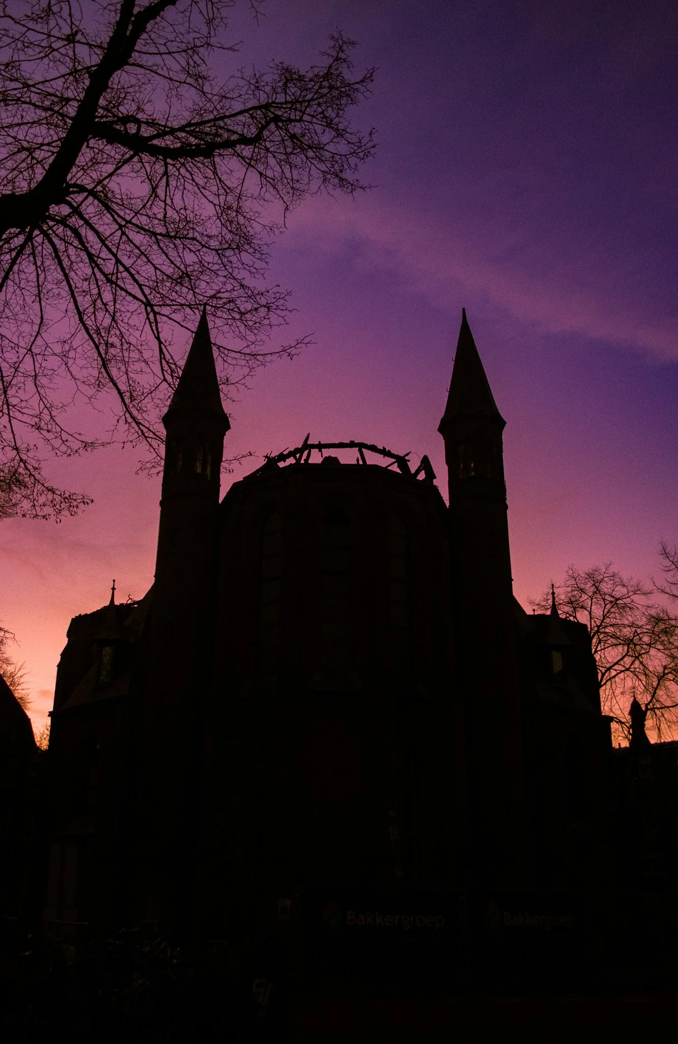 The silhouette of a castle with two tall, pointed towers against a purple and pink sunset sky, with leafless trees in the foreground.