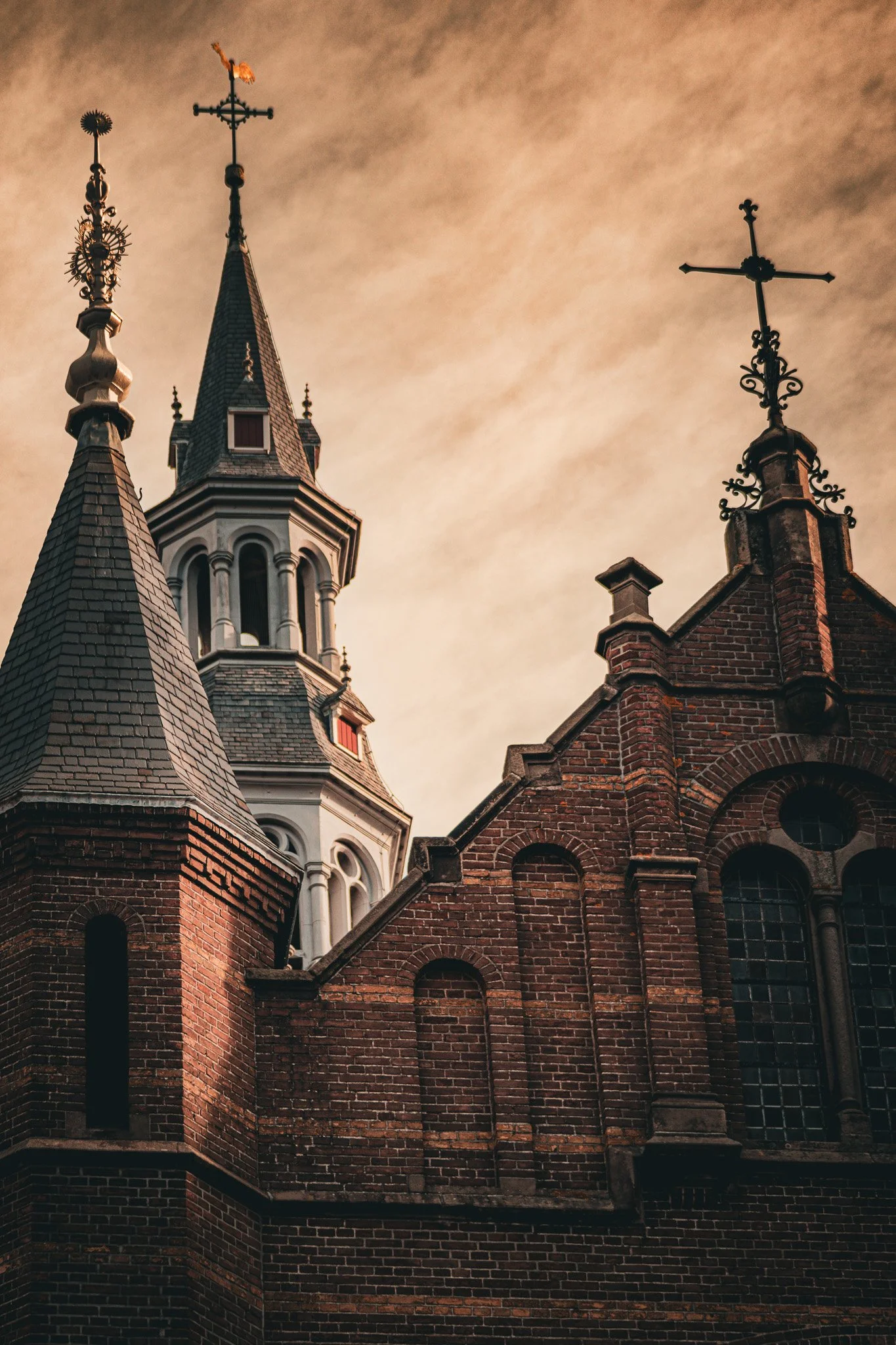 Close-up of church steeples and brick roof against cloudy sky.