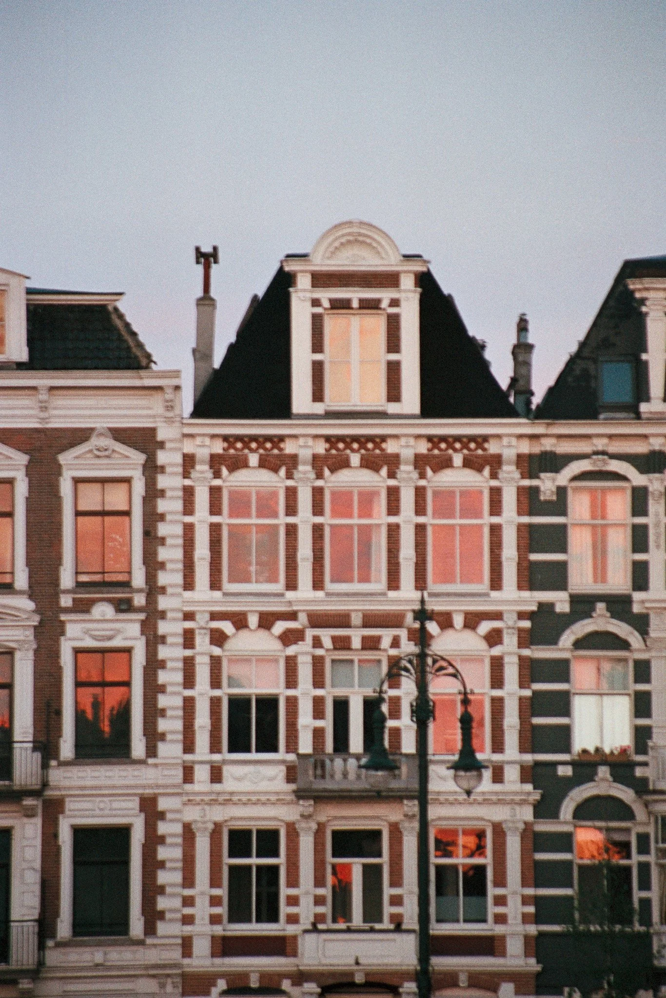 Historical European-style buildings with ornate facades, large windows with red and orange reflections, and a decorative street lamp in front.