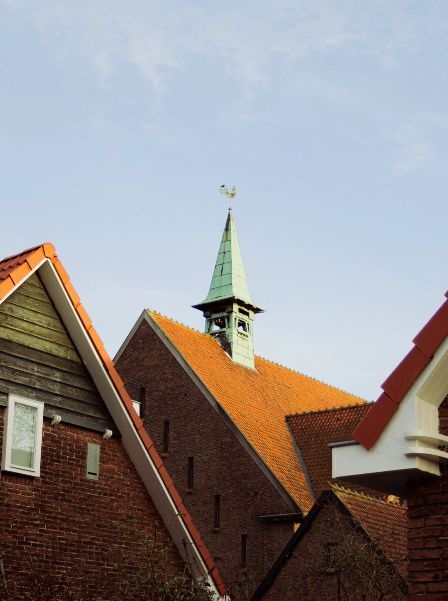 A view of rooftops with red tiles and a church steeple against a blue sky.