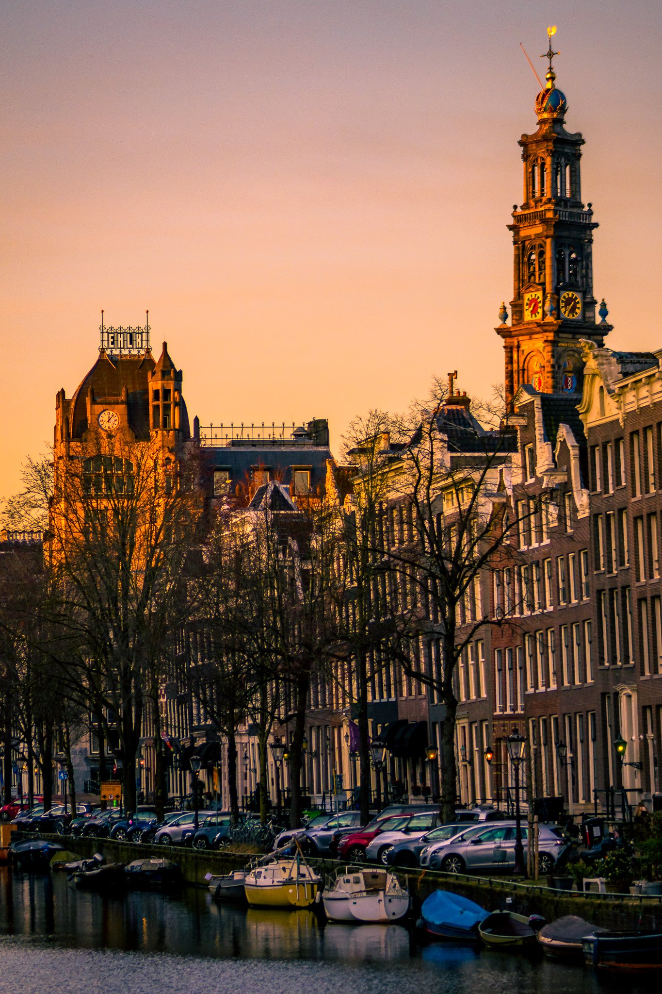 Sunset over canals with boats, historic buildings, and colorful sky in Amsterdam, Netherlands.