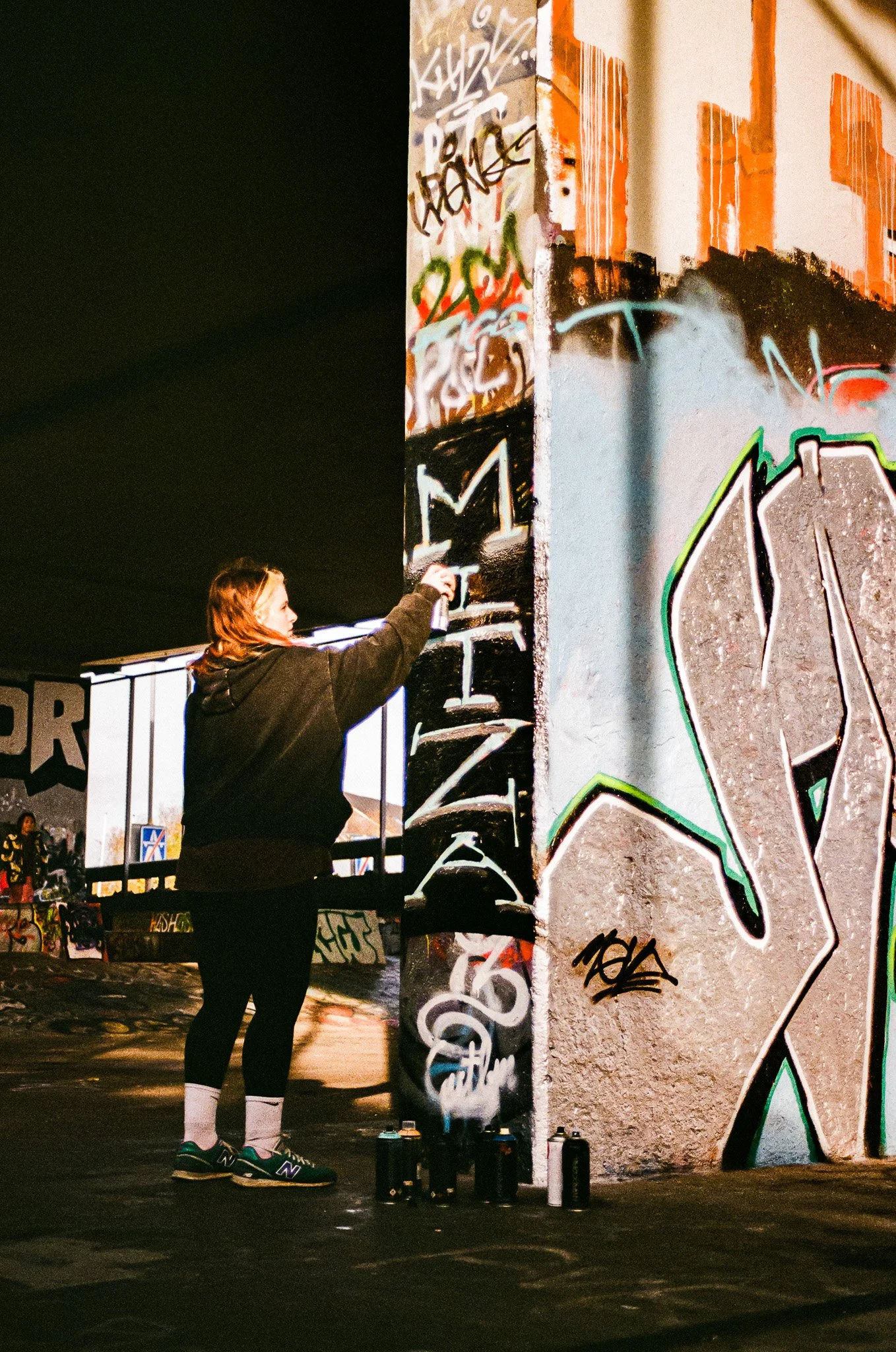 A woman spray painting graffiti on a wall at night.