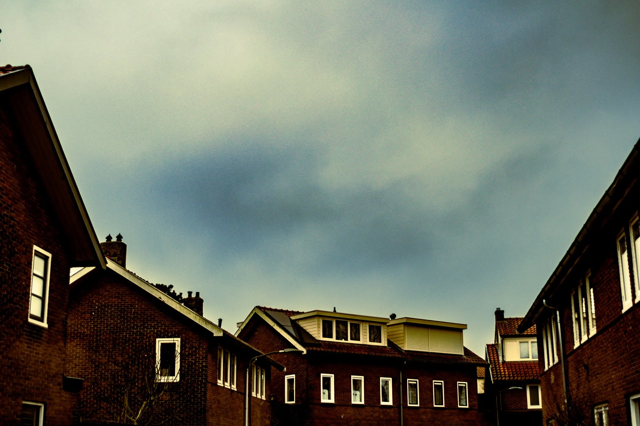 View of multiple brick residential buildings with sloped roofs under a cloudy sky.
