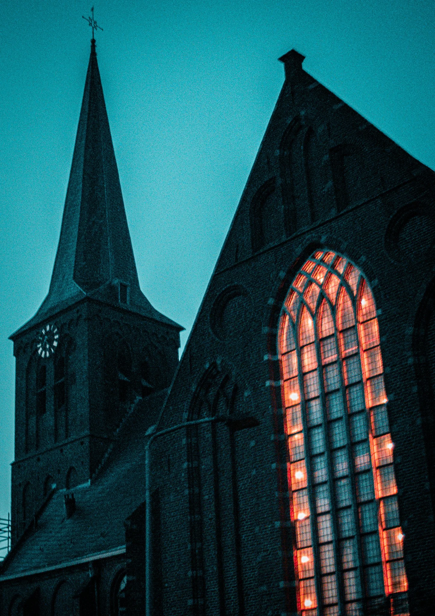 A church with a tall steeple and large illuminated stained glass windows at night.