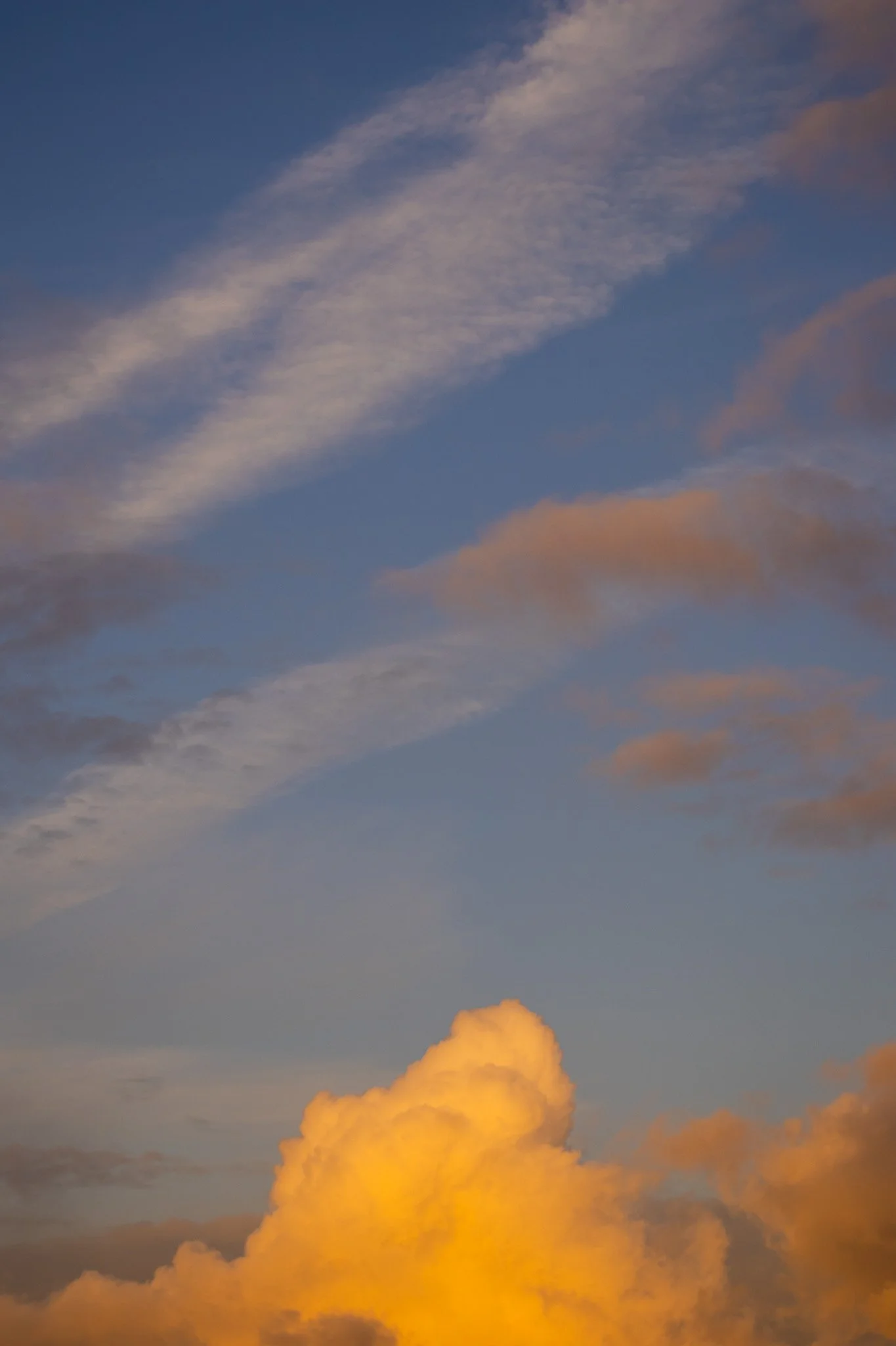Sky with clouds at sunset, featuring a large, bright orange cloud near the bottom and wispy clouds higher in the sky.
