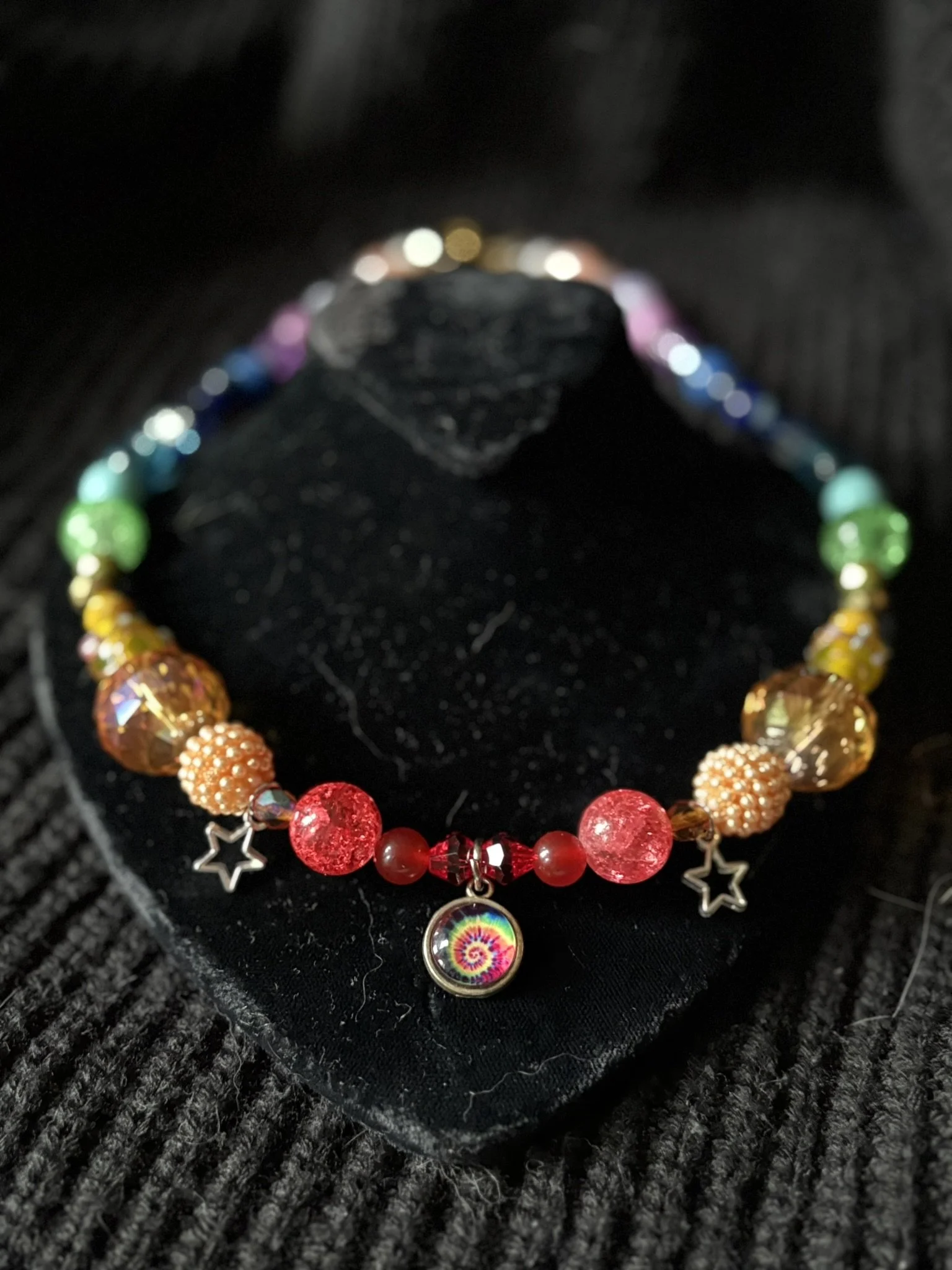 Colorful beaded necklace with star charms and a round rainbow-colored pendant, displayed on black fabric.
