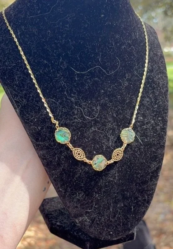 Gold necklace with five oval-shaped opal stones displayed on a black velvet bust.