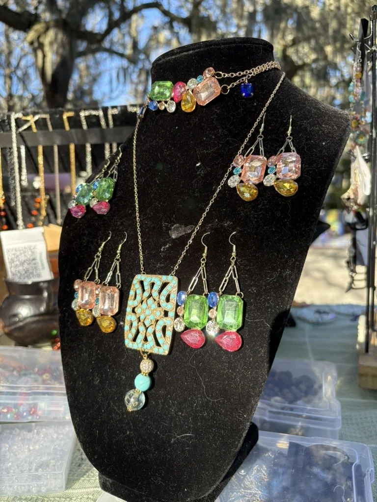 Display of colorful jewelry including earrings, necklaces, and a bracelet on a black bust at an outdoor market.
