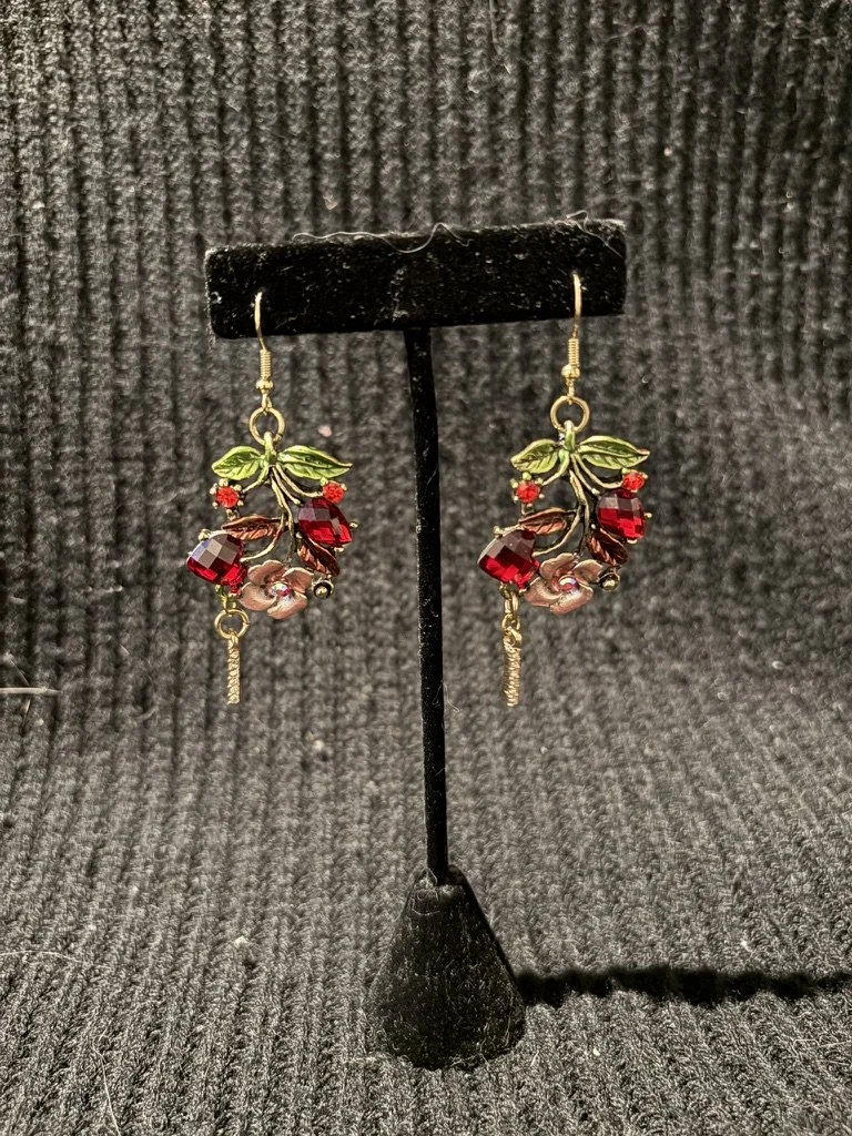 Earrings with a leaf design and red gemstones displayed on a black stand.