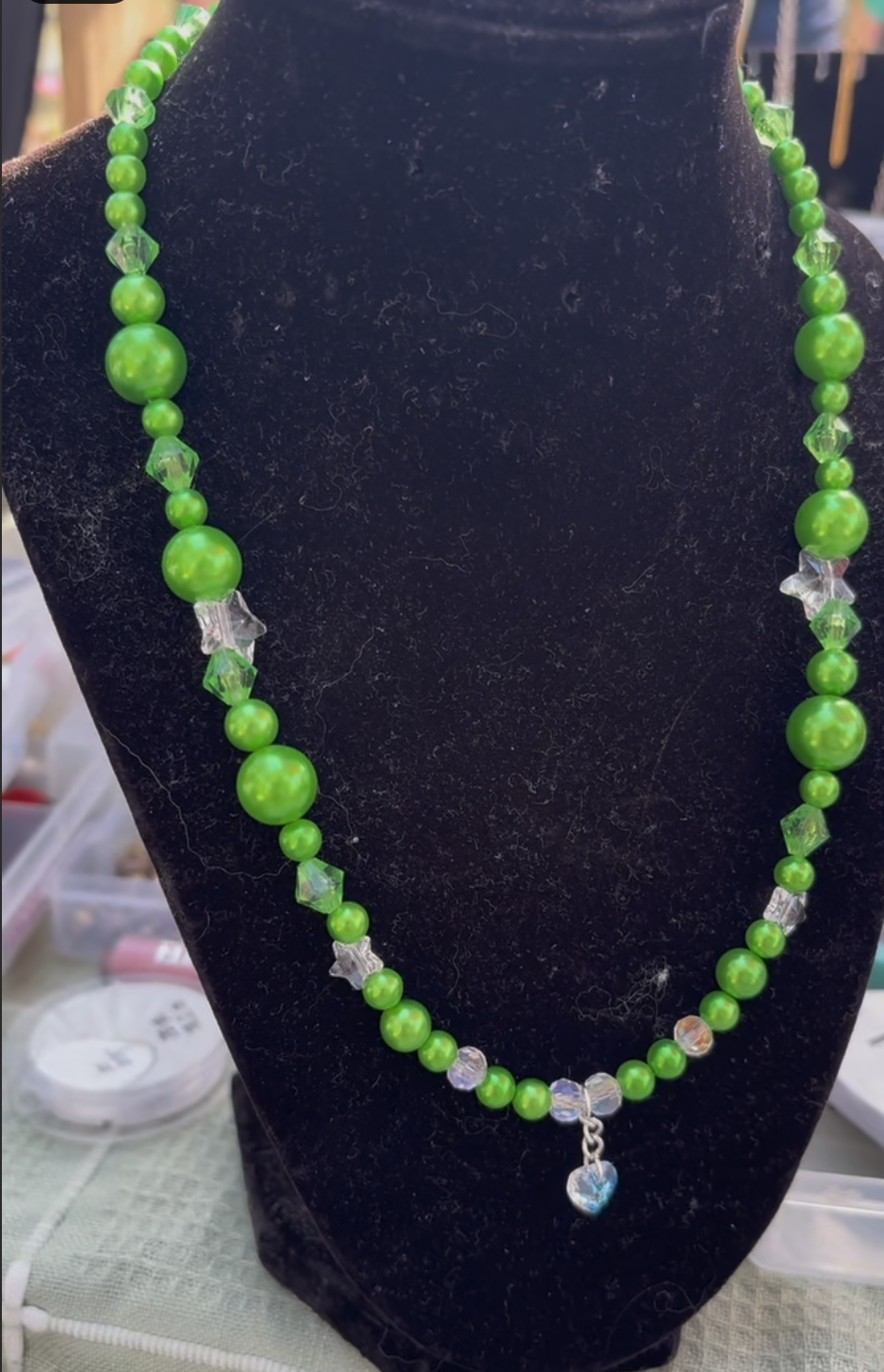 Green beaded necklace with a heart-shaped pendant displayed on a black jewelry stand.
