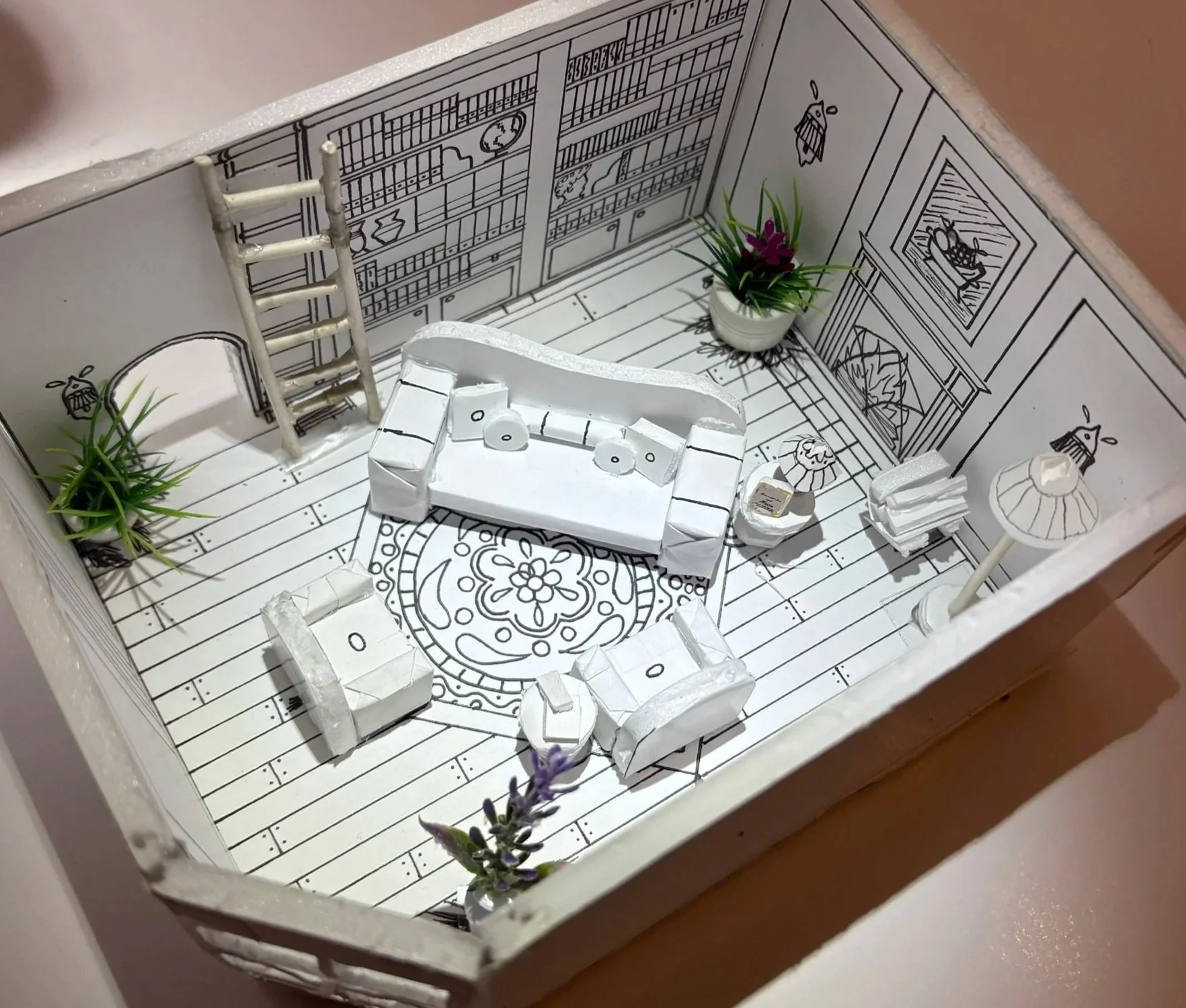 Miniature room with black and white line drawings of furniture and decor on the walls and floor, containing small plants, a couch made of white paper, and tiny paper accessories.