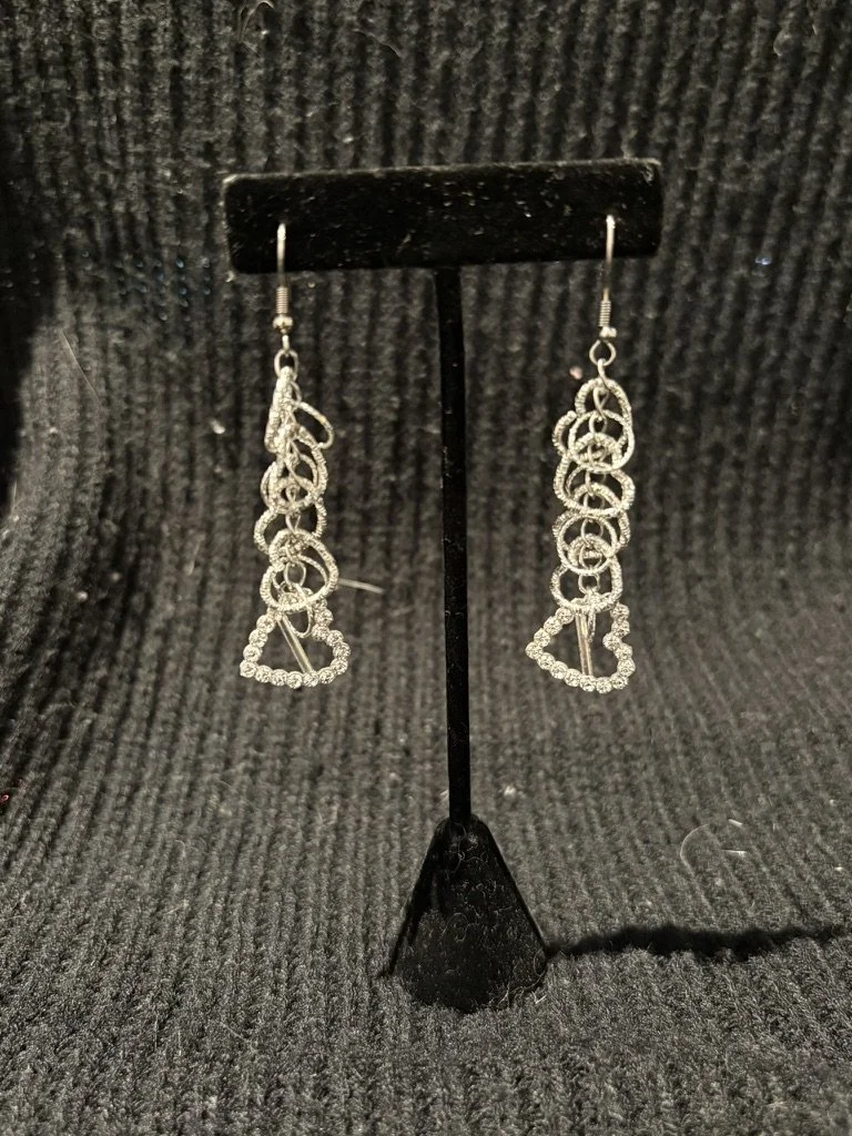 Silver earrings with cascading circular and triangular shapes displayed on a black stand against a textured black background.