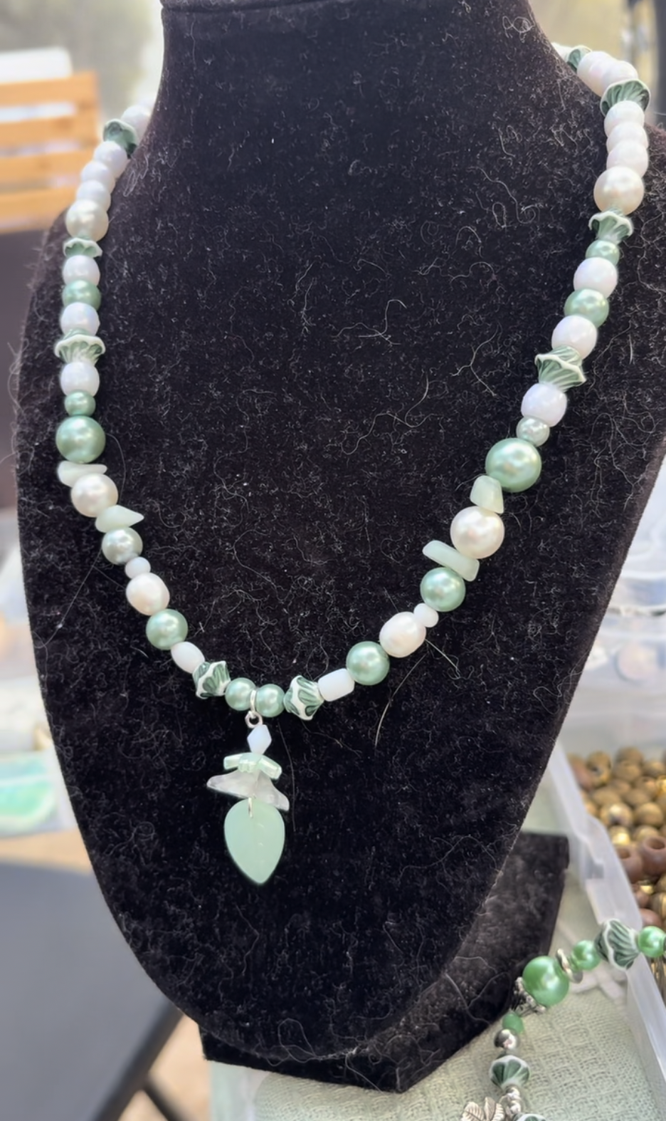 Green and white beaded necklace with a leaf pendant displayed on a black velvet bust form.