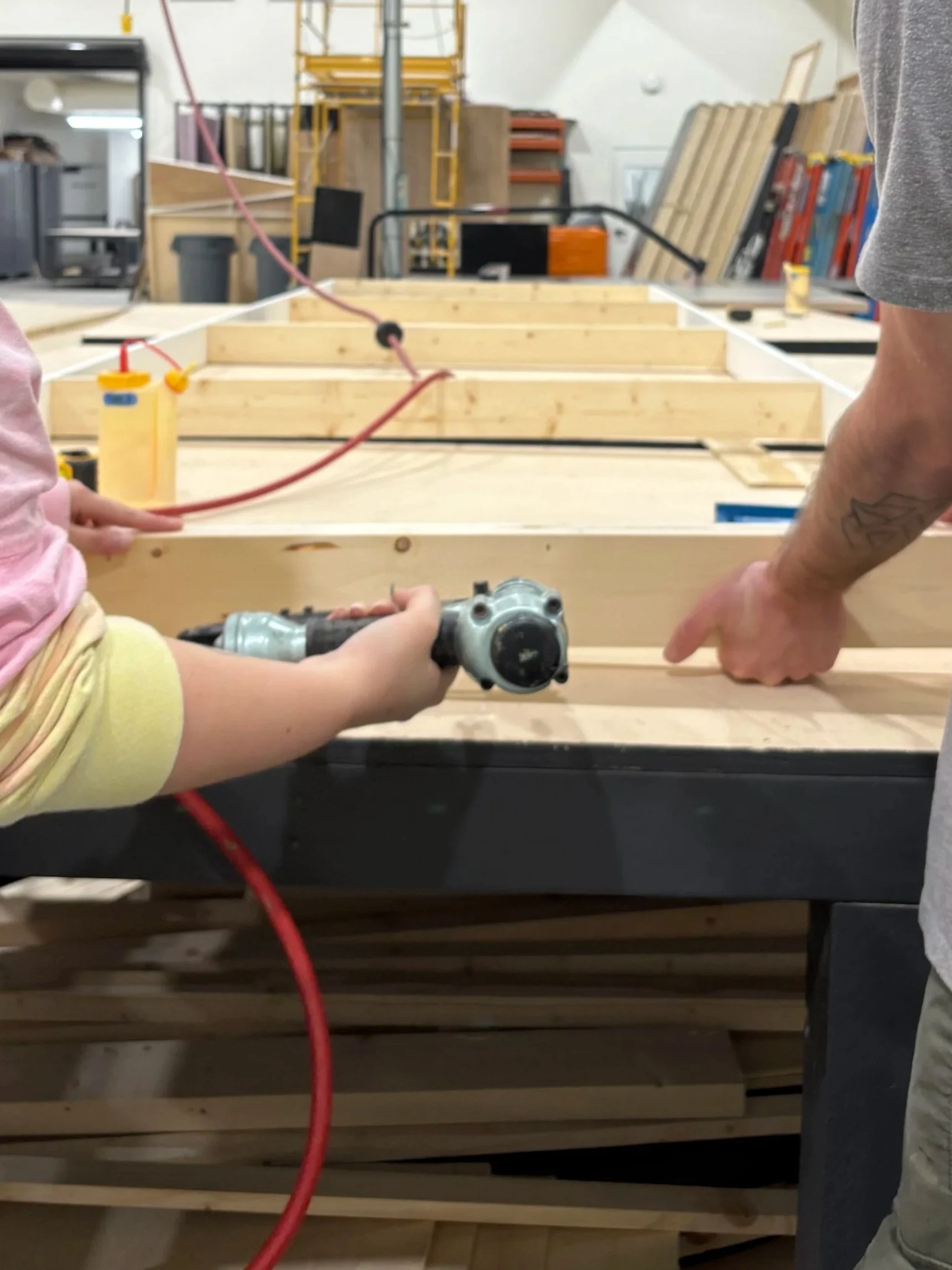 People working on a woodworking project on a wooden table in a workshop.