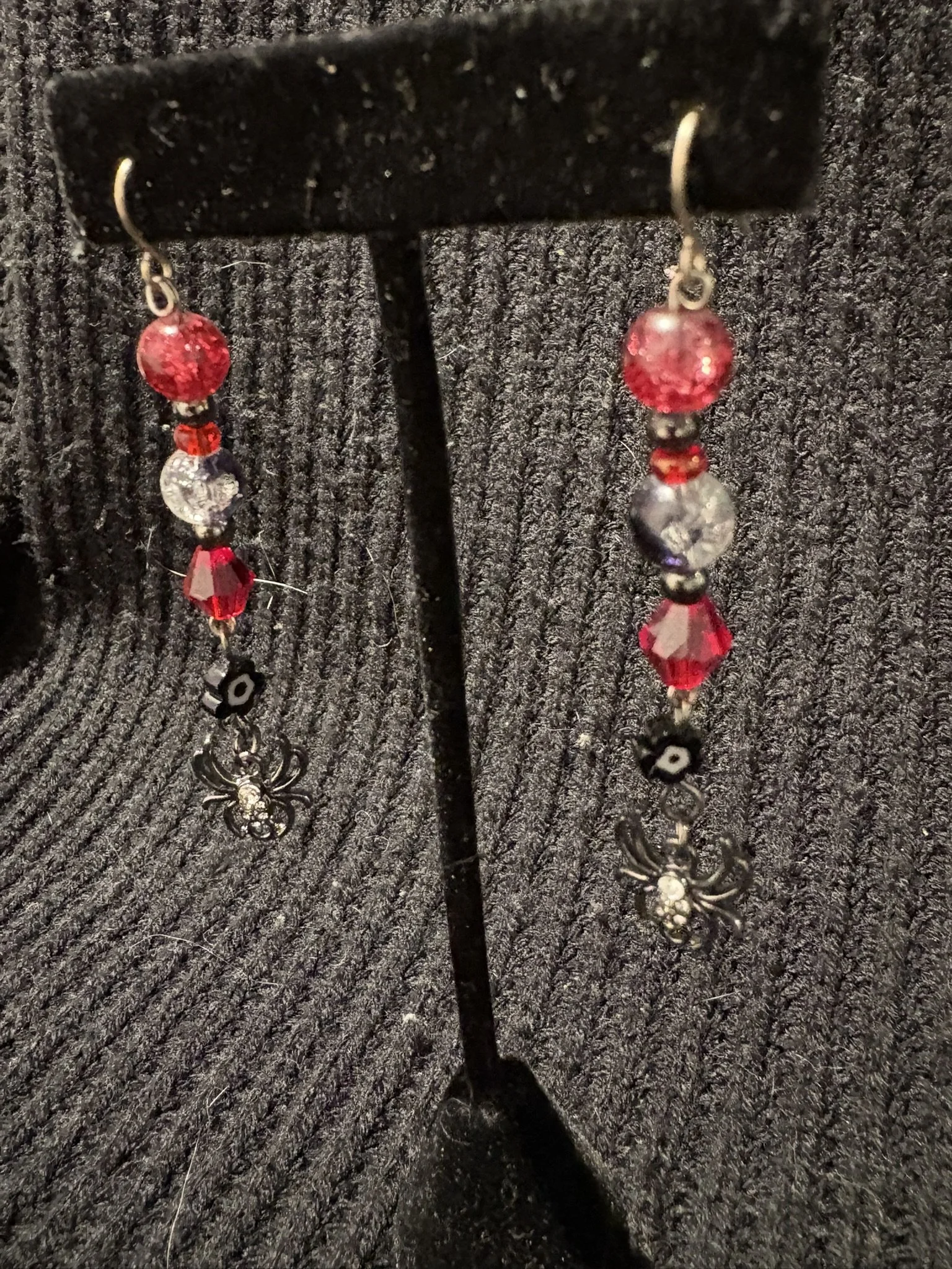 Red and clear beaded earrings hanging from a black display stand on a dark textured background.