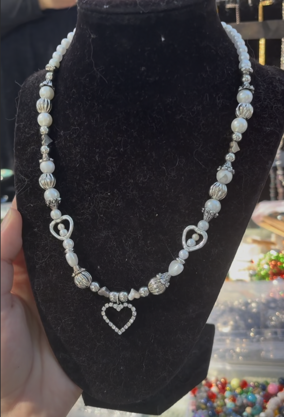 A pearl necklace with heart-shaped pendants displayed on a black velvet stand.