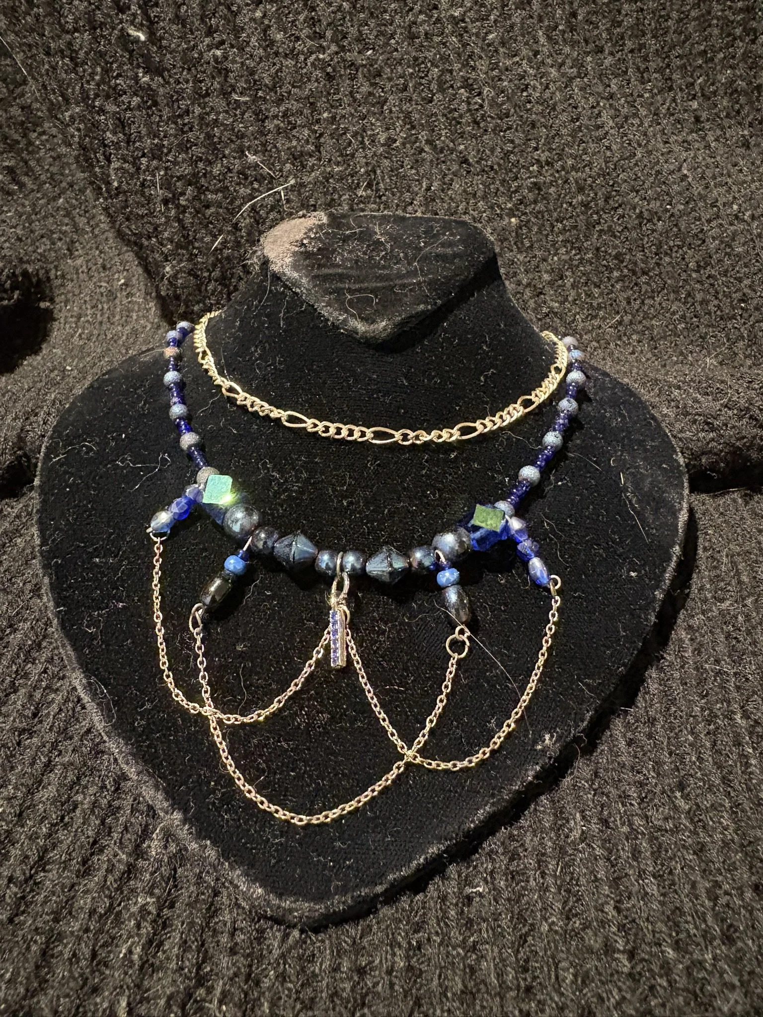 Various necklaces and chains displayed on a black velvet bust against a dark background.