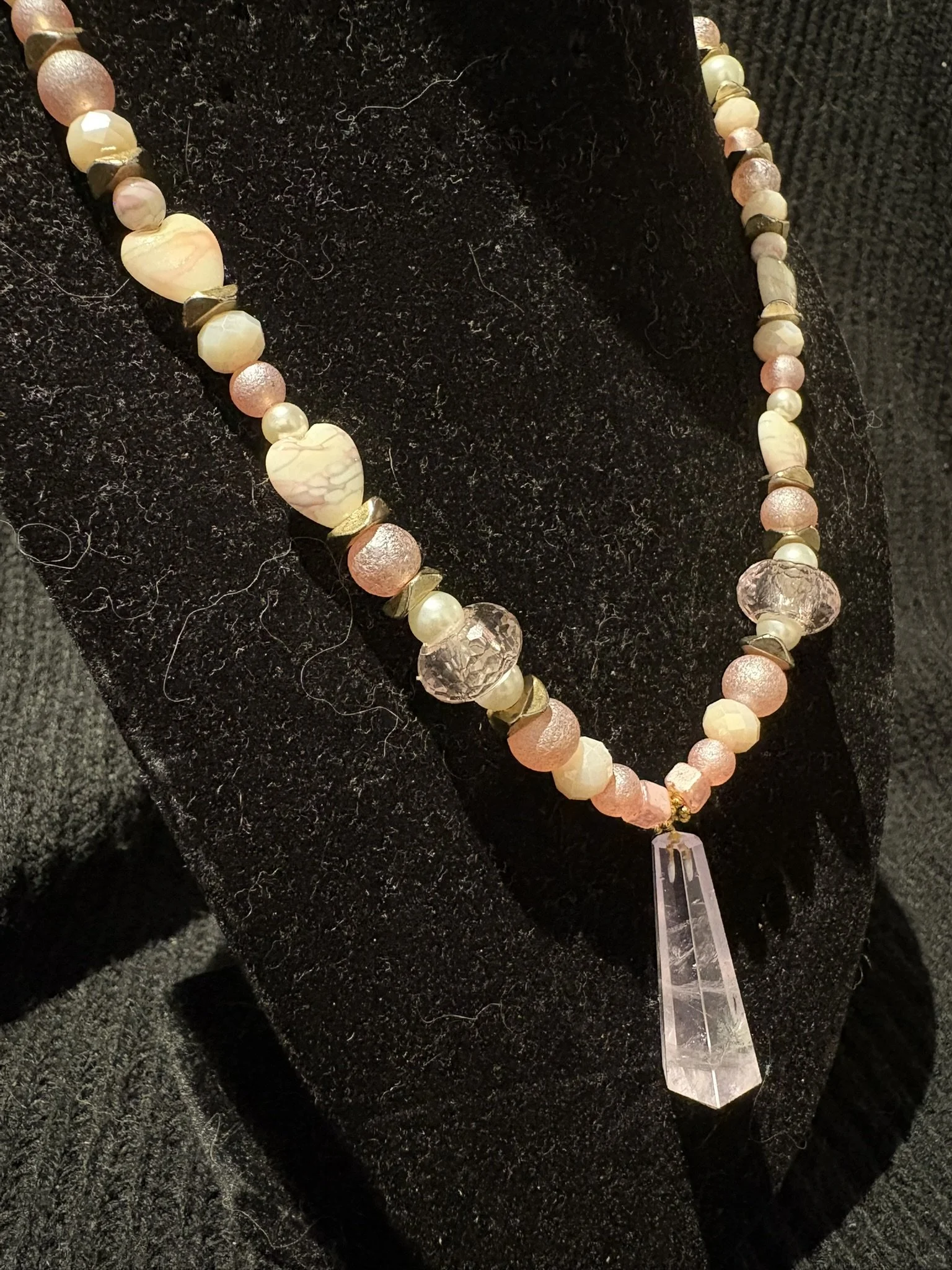 A beaded necklace with a large clear quartz pendulum displayed on a black textured surface.