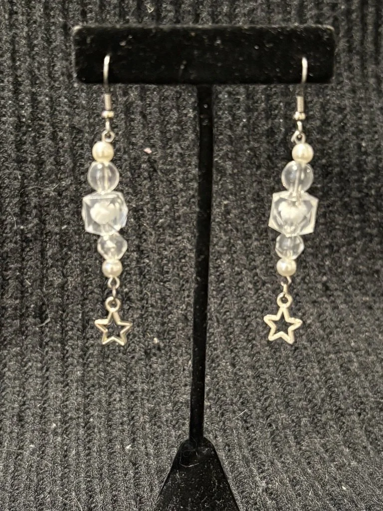 Drop earrings featuring beads and small star charms hanging from silver hooks, displayed on a black stand.