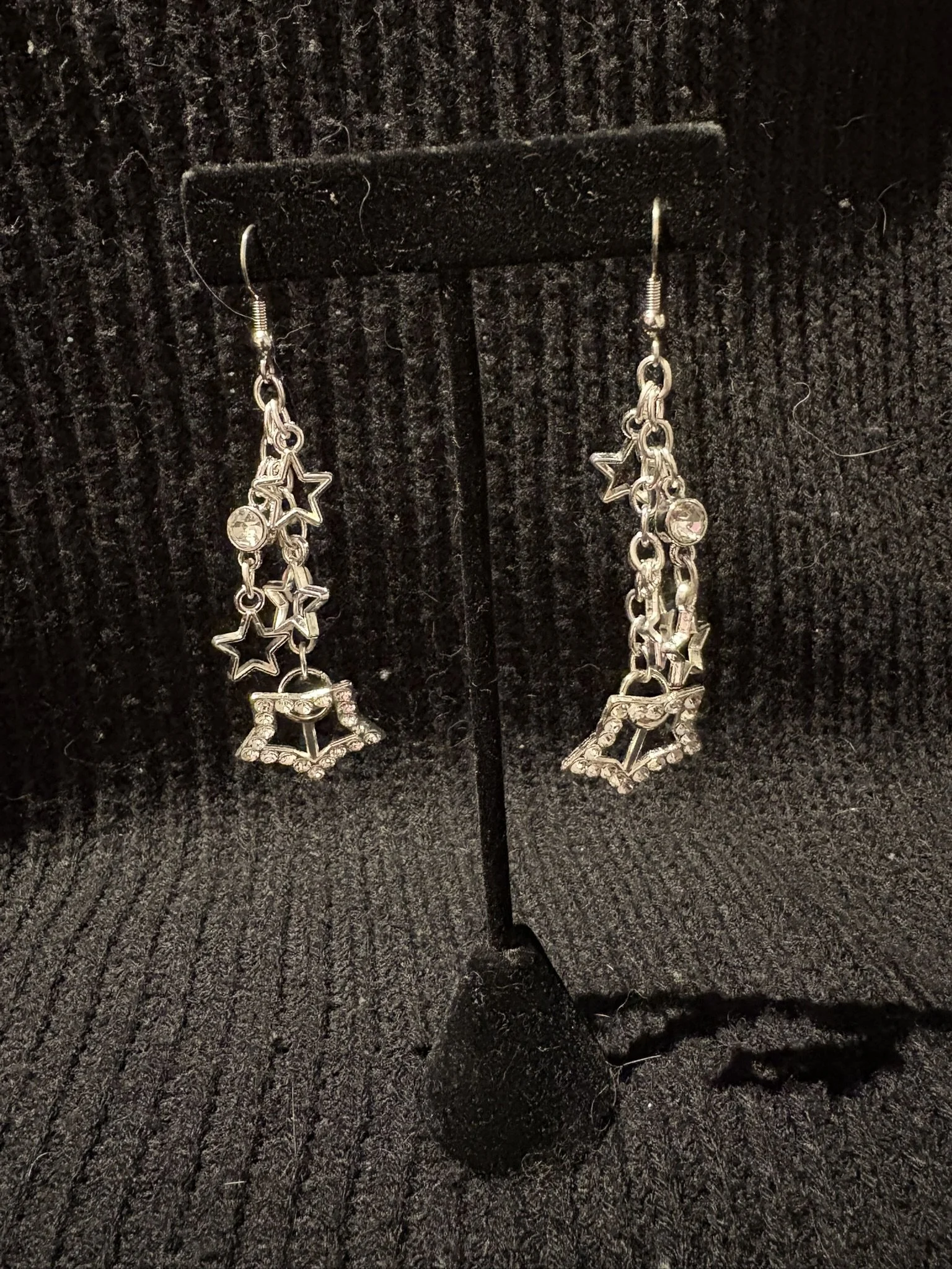 Pair of dangling earrings with star-shaped and circular elements on a black textured background.
