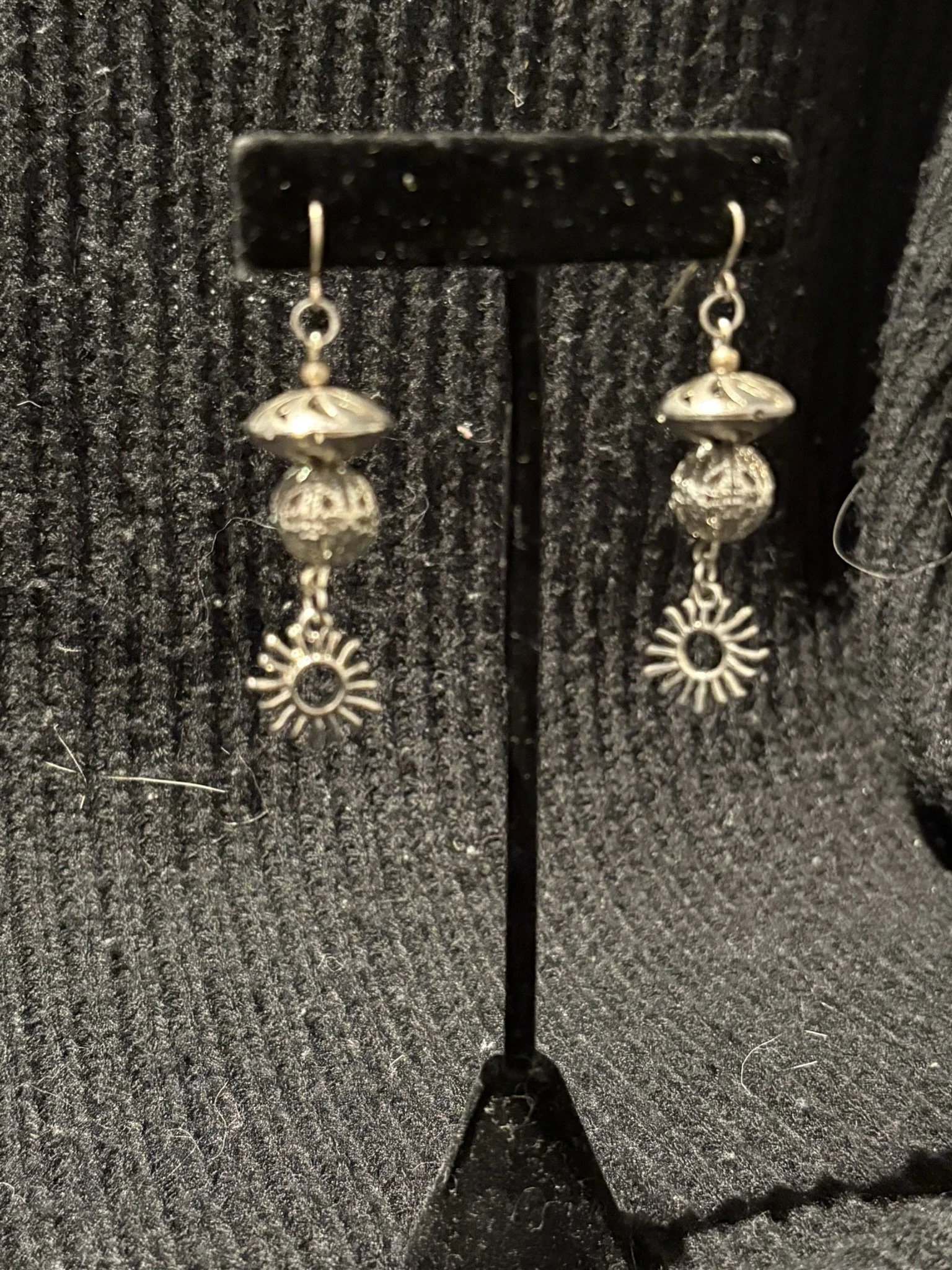A pair of dangling earrings hanging on a black jewelry display, with a textured black background.